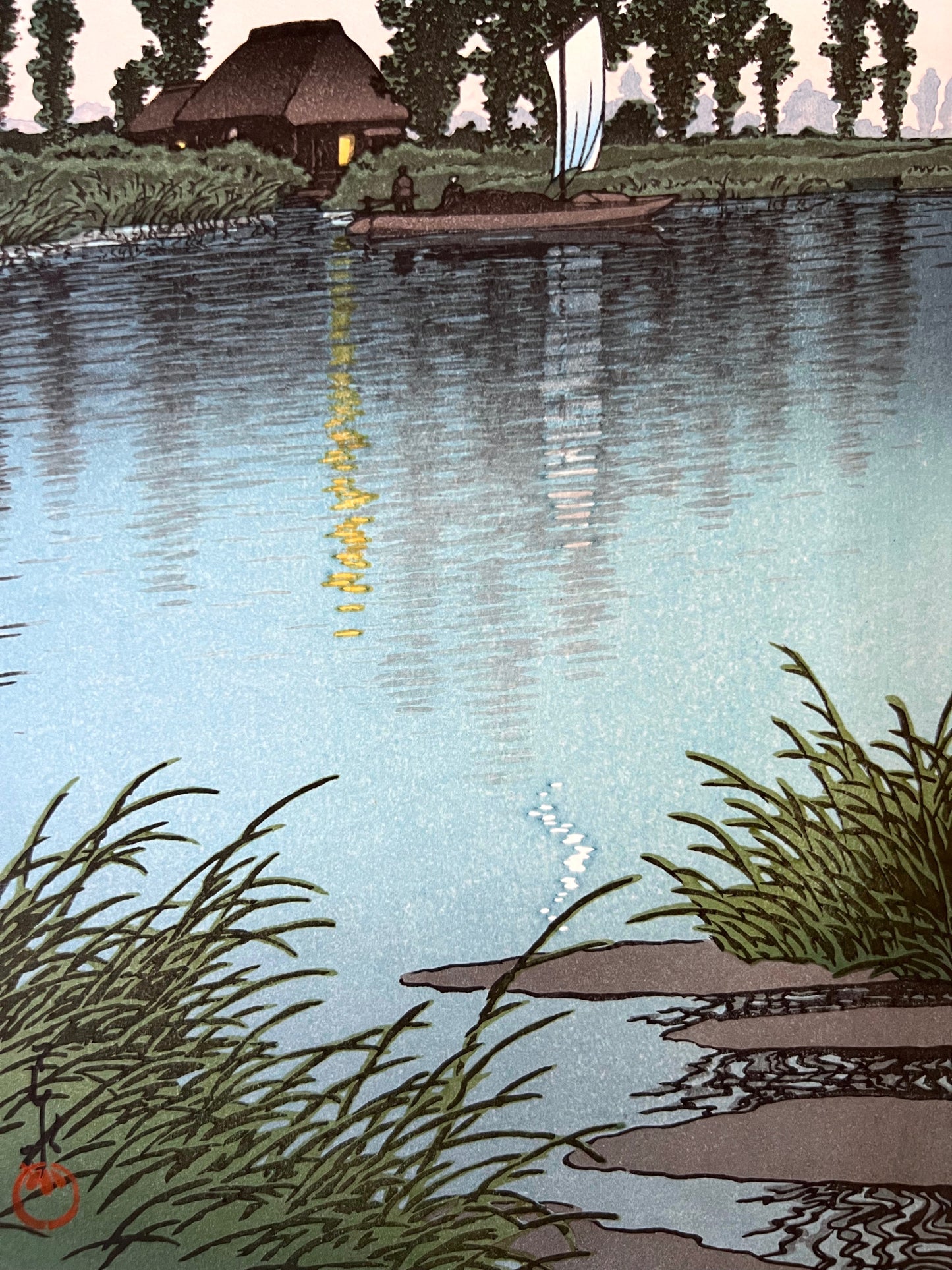 estampe japonaise d'un paysage nocturne de Hasui, avec un croissant de lune, une rivière, un bateaux à voile passant devant une chaumière éclairée, reflet de la lumière dans l'eau