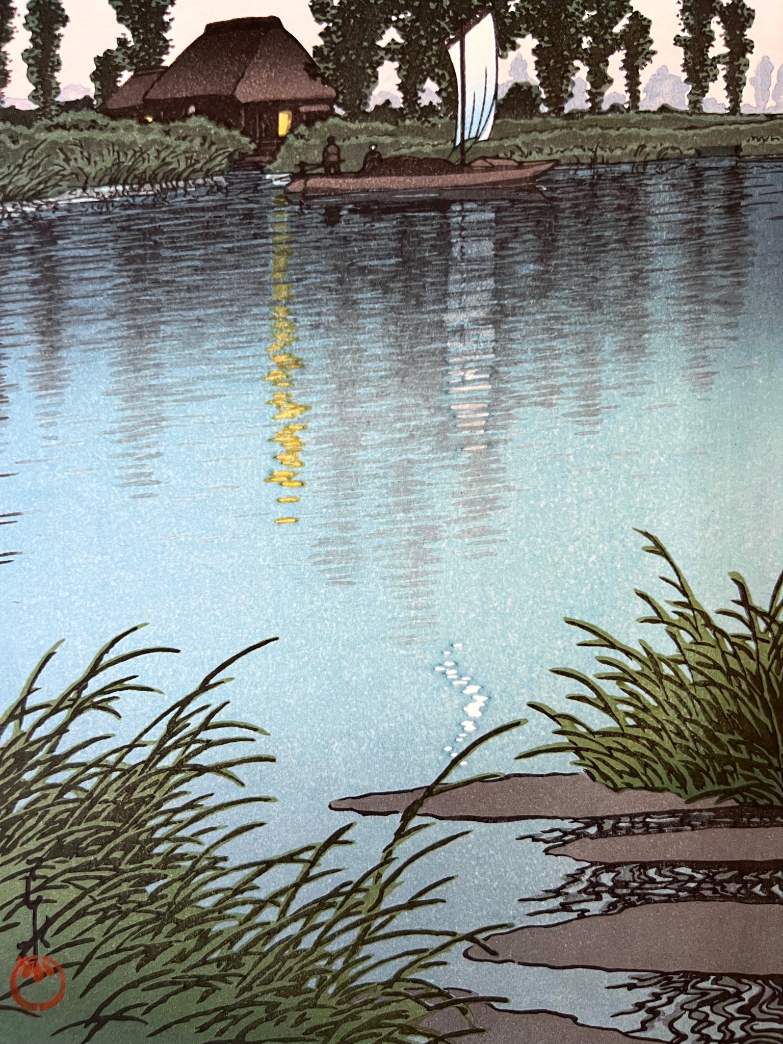 estampe japonaise d'un paysage nocturne de Hasui, avec un croissant de lune, une rivière, un bateaux à voile passant devant une chaumière éclairée, reflet de la lumière dans l'eau