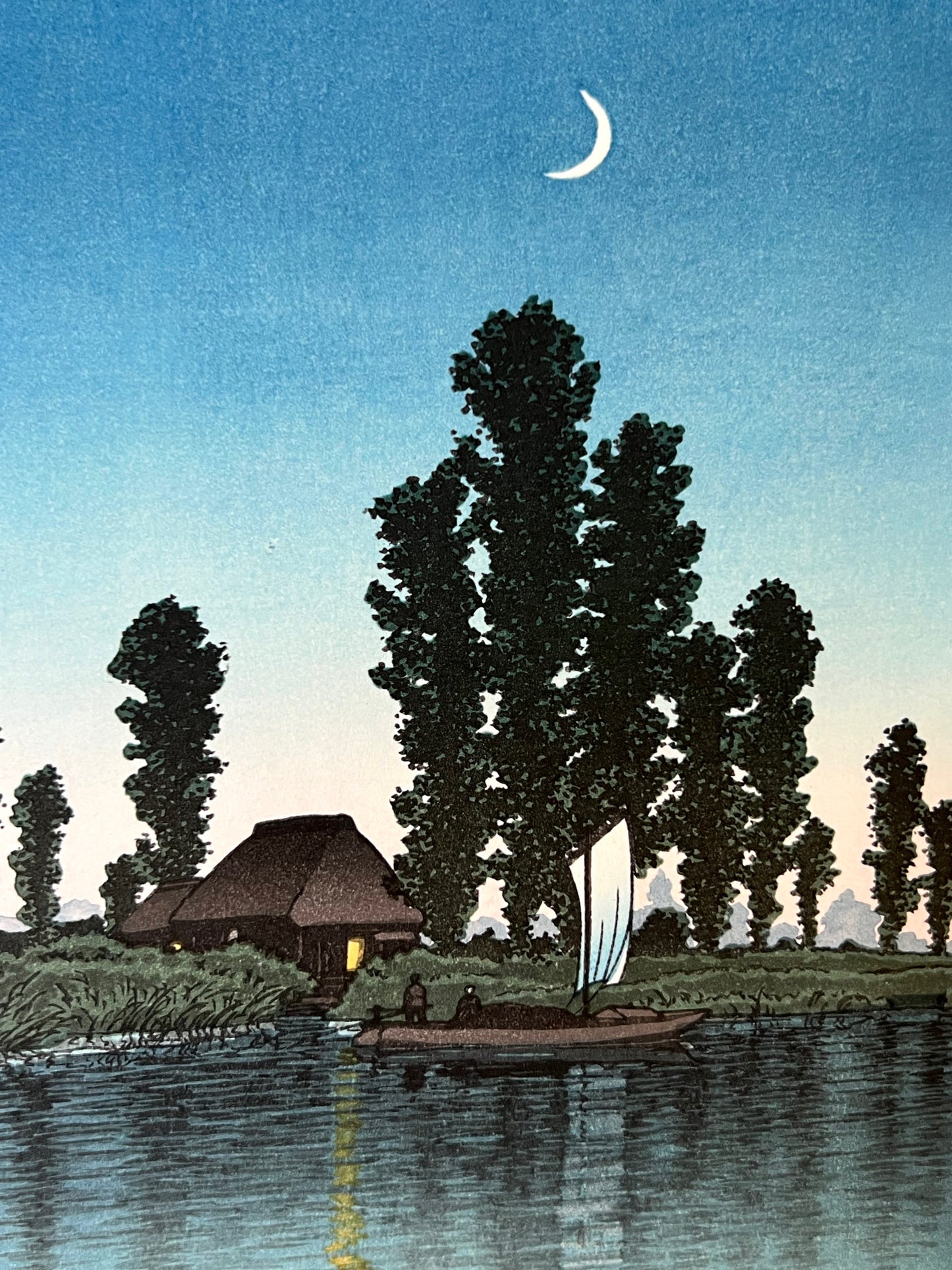 estampe japonaise d'un paysage nocturne de Hasui, avec un croissant de lune, une rivière, un bateaux à voile passant devant une chaumière éclairée, gros plan sur la barque