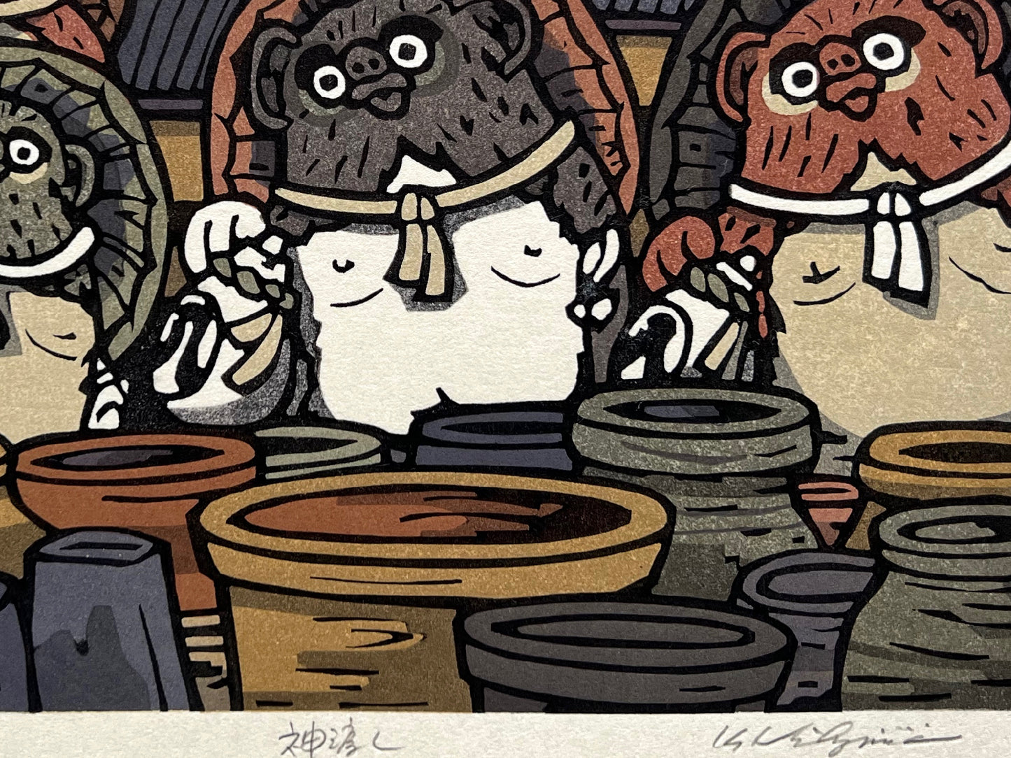 estampe japonaise groupe de tanuki devant des jarres en terre, toit des maisons et ciel jaune orange en arrière plan, gros plan sur la signature de l'artiste