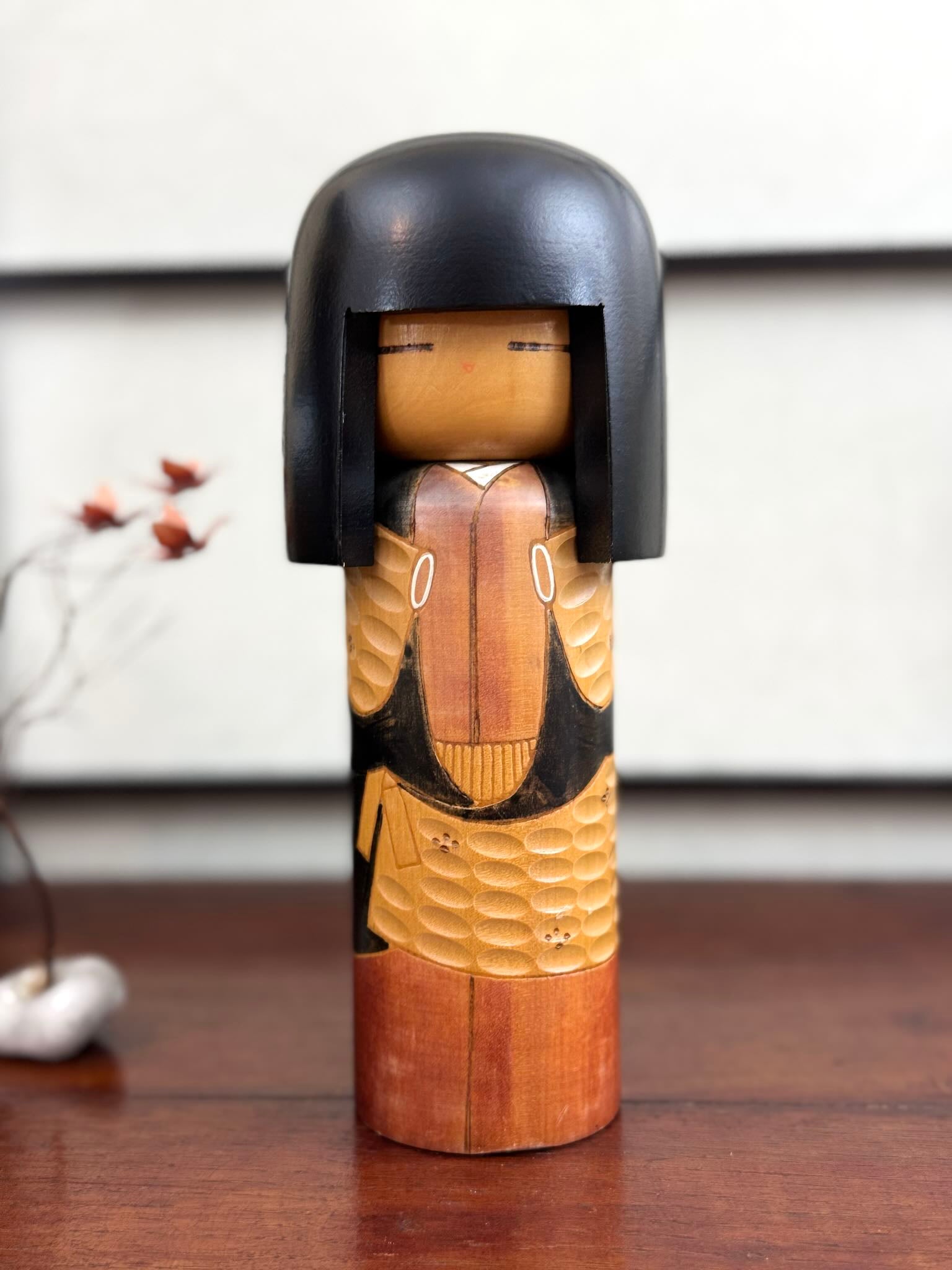 Kokeshi vintage Shinonome de Kisaku avec kimono sculpté en relief et coiffure noire, vu de face.