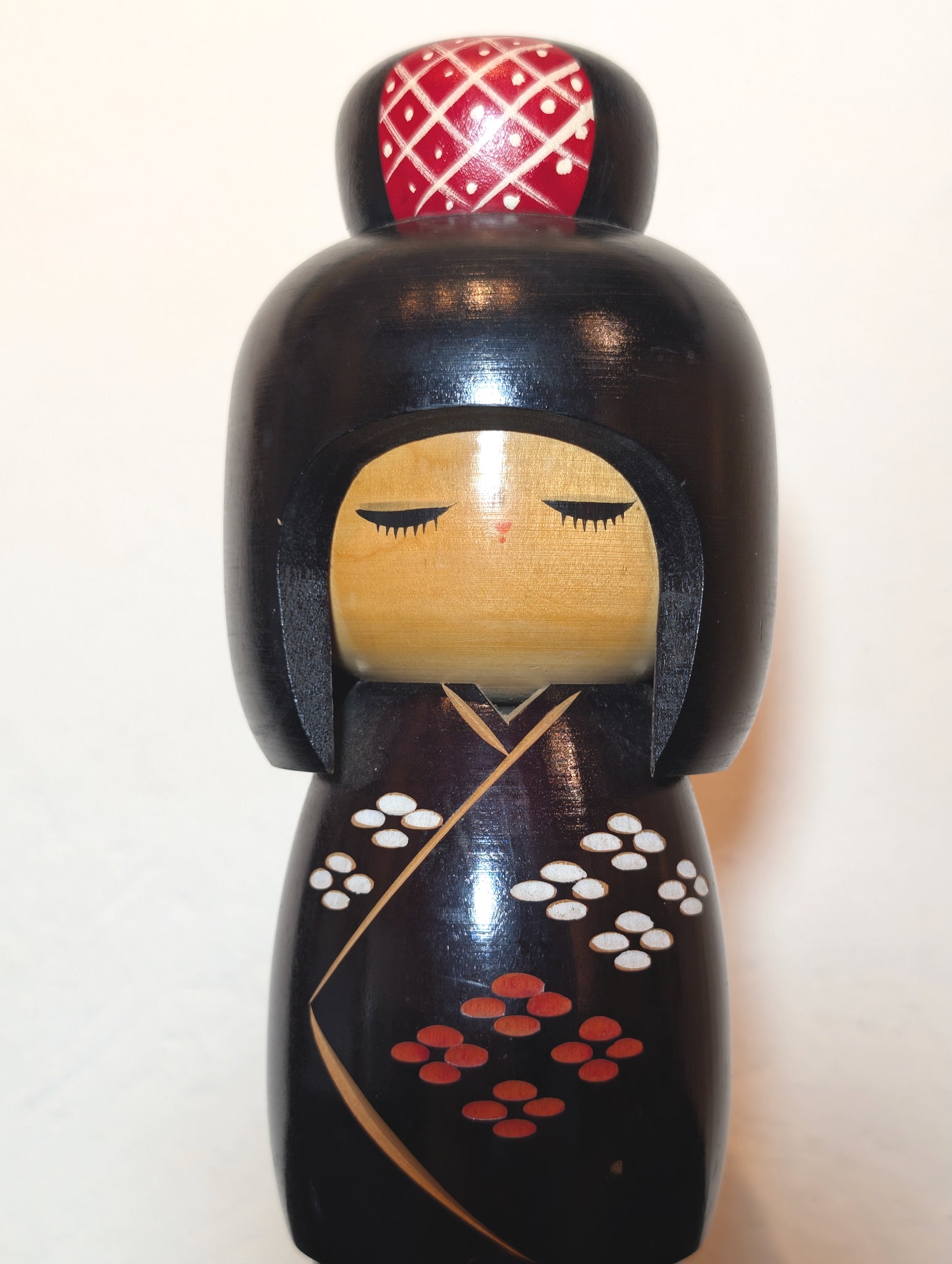 kokeshi de Kunio Miyagawa, kimono noir avec fleurs de cerisier rouges et blanches, gros plan sur le visage surmonté d'un chignon