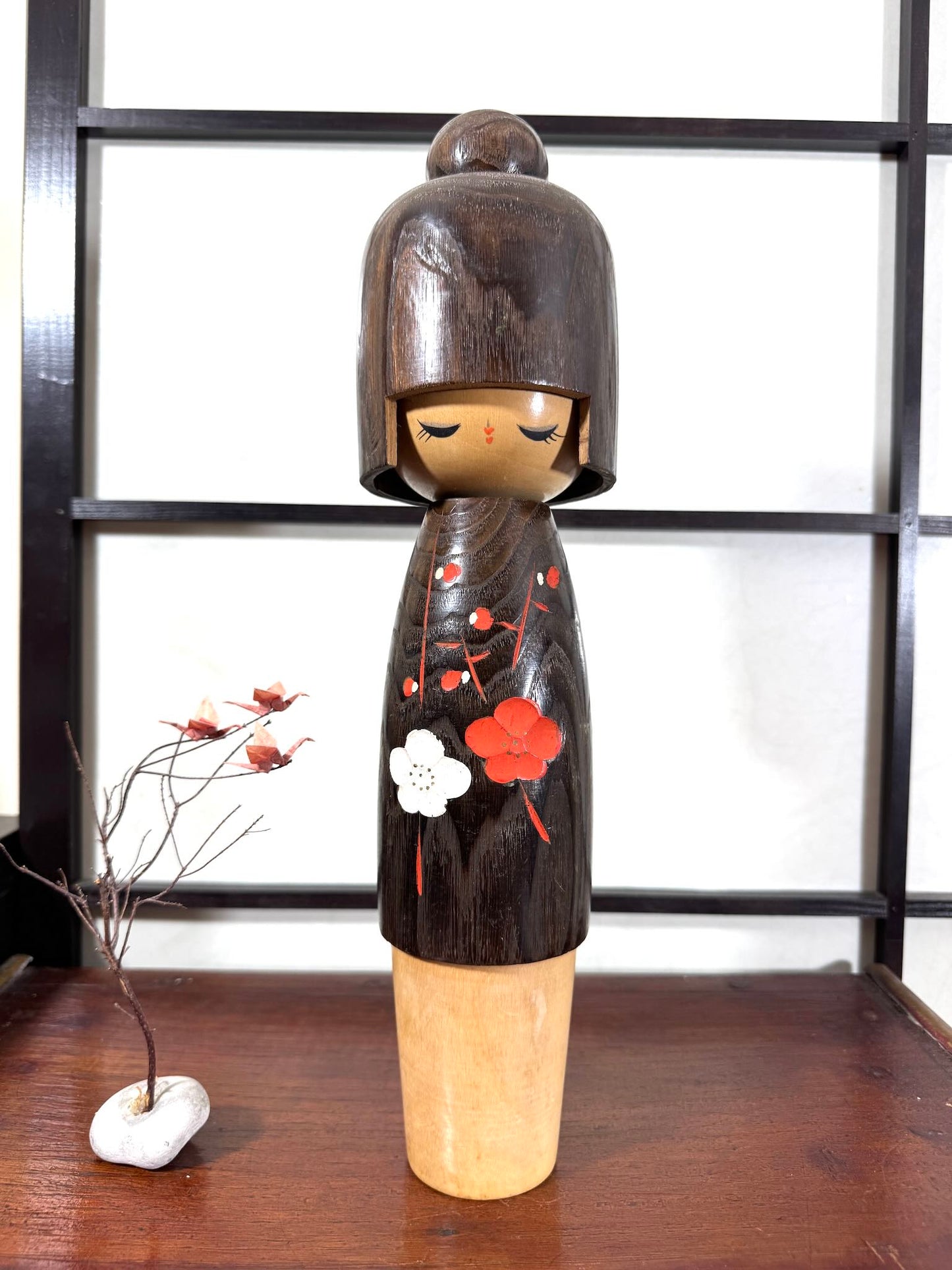 Grande kokeshi Usaburō Koigokoro en bois sombre avec fleurs de prunier rouges et blanches, vu de face.