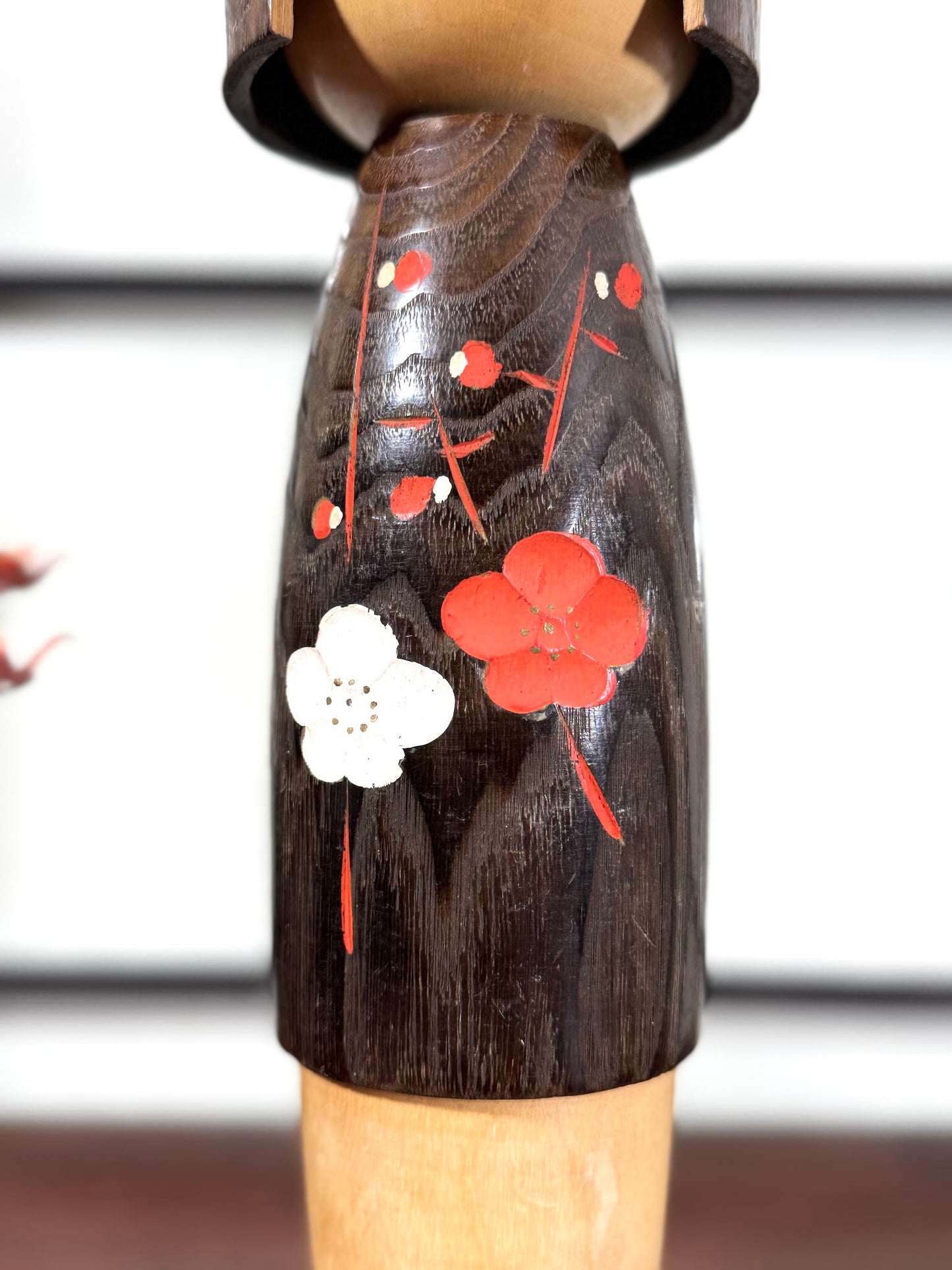 Grande kokeshi Usaburō Koigokoro en bois sombre avec fleurs de prunier rouges et blanches, gros plan sur les fleurs gravées et peintes.