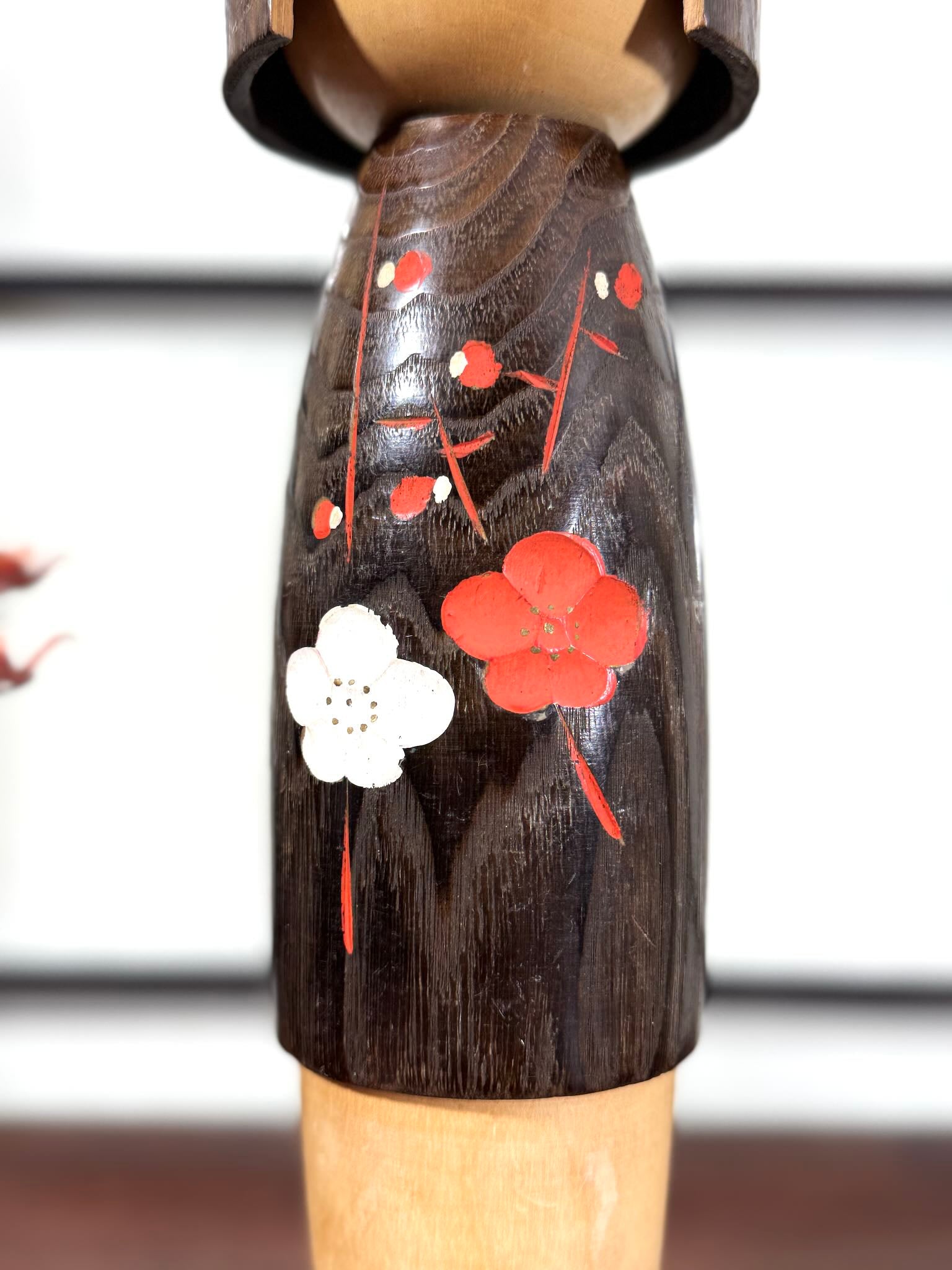 Grande kokeshi Usaburō Koigokoro en bois sombre avec fleurs de prunier rouges et blanches, gros plan sur les fleurs gravées et peintes.