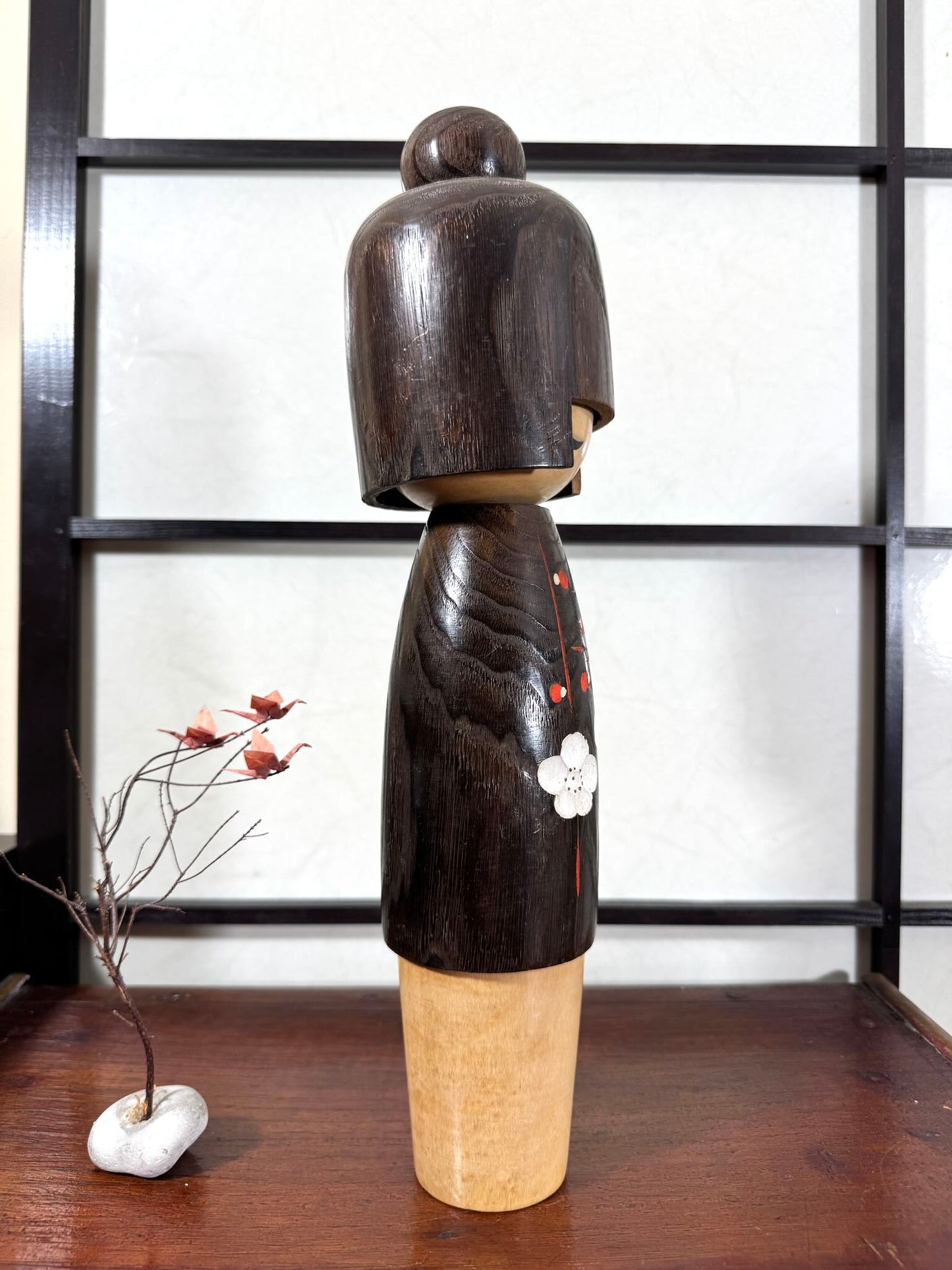 Grande kokeshi Usaburō Koigokoro en bois sombre avec fleurs de prunier rouges et blanches, vu du profil droit.