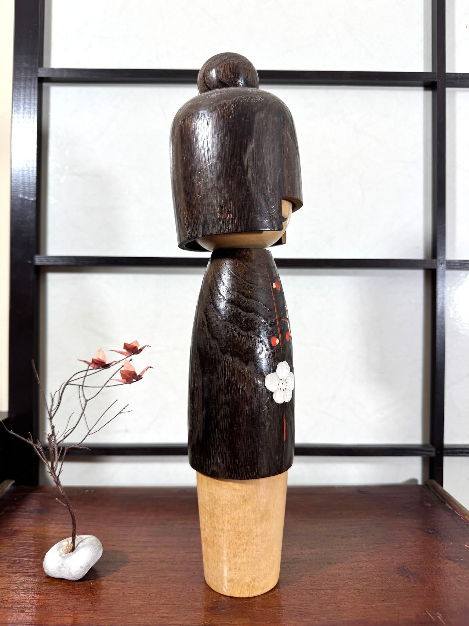Grande kokeshi Usaburō Koigokoro en bois sombre avec fleurs de prunier rouges et blanches, vu du profil droit.