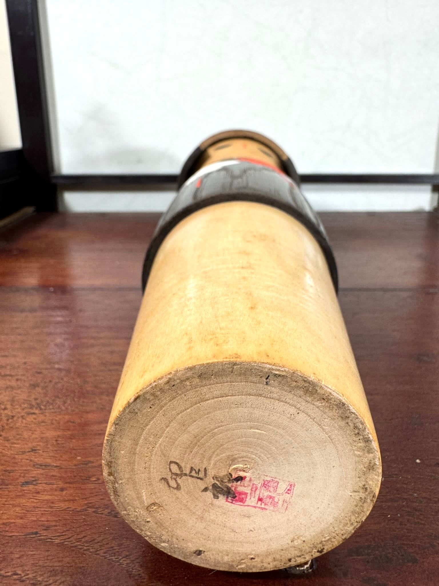 Grande kokeshi Usaburō Koigokoro en bois sombre avec fleurs de prunier rouges et blanches, vu de la signature au dessous.