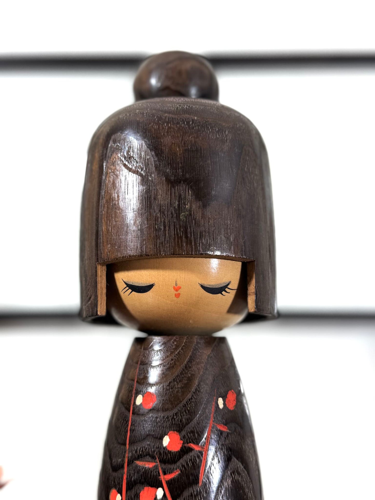 Grande kokeshi Usaburō Koigokoro en bois sombre avec fleurs de prunier rouges et blanches, gros plan sur le visage aux yeux mi-clos