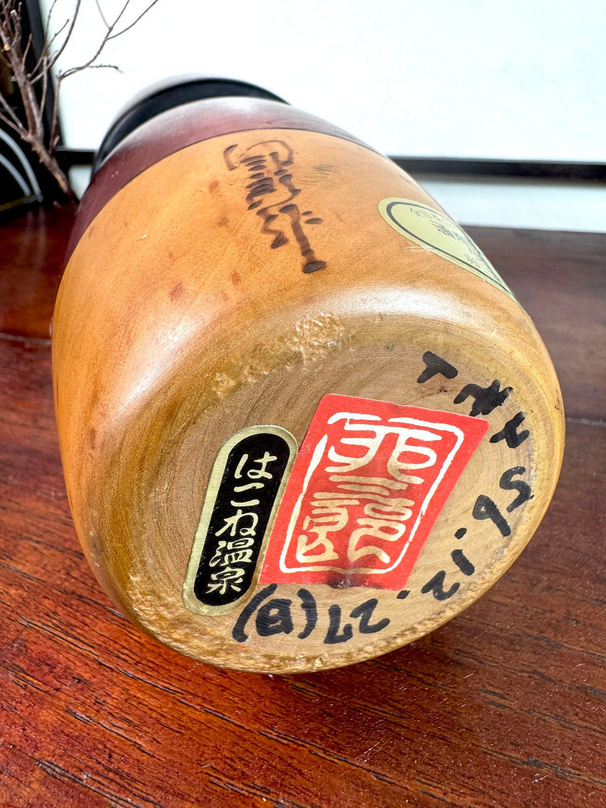 Kokeshi vintage Usaburō de 25 cm ornée de camélias rouges, le dessous avec signature artiste, étiquette onsen Hakone et date d'achat 56.12.27