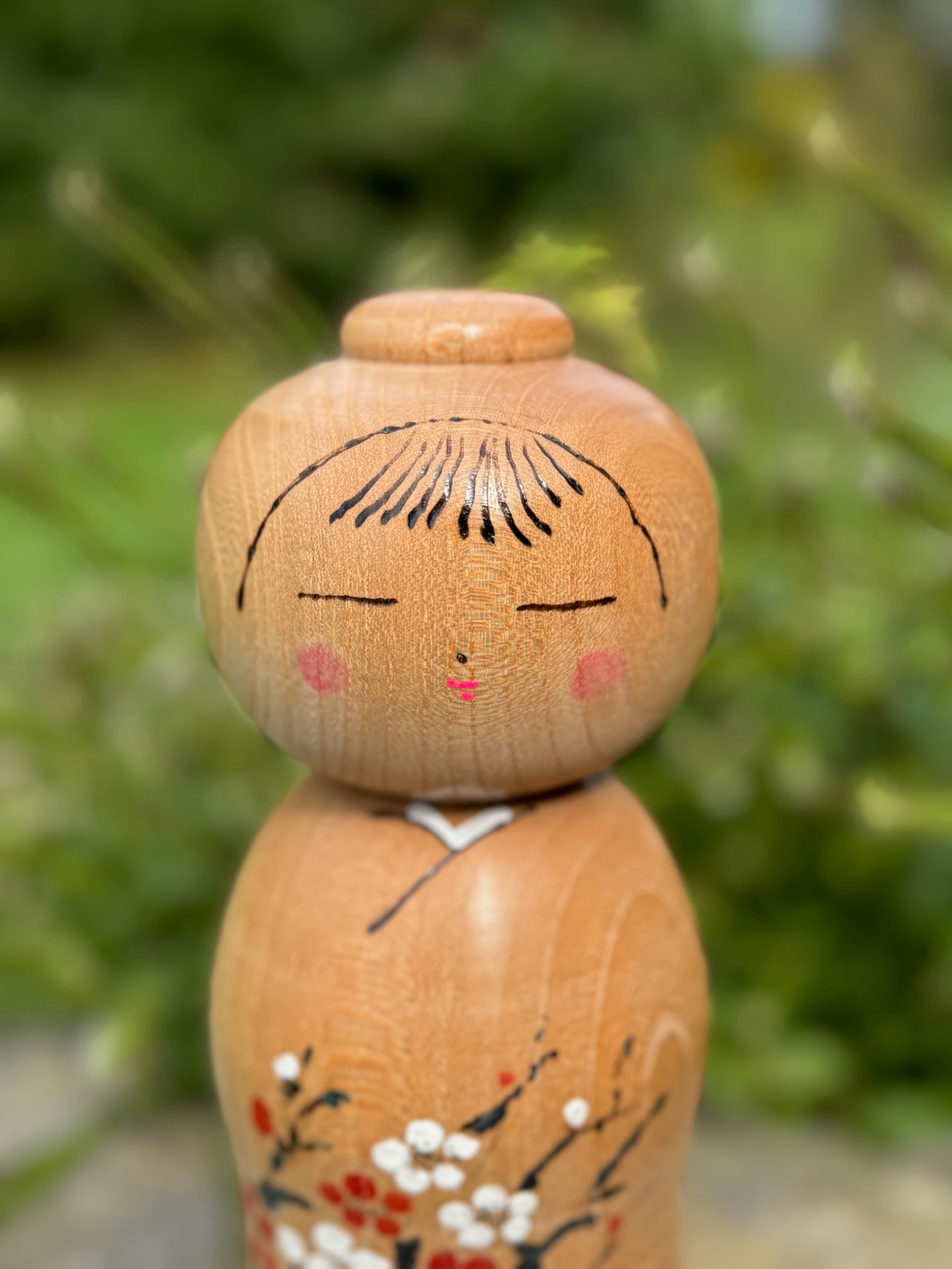 kokeshi poupée japonaise en bois de Yuho Ouchi, branche de prunier rouge et blanc en fleur, gros plan sur le visage souriant
