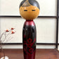 Kokeshi vintage de Sato Norio en laque noire et rouge avec branche de prunier en fleurs, vu de face
