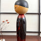 Kokeshi vintage de Sato Norio en laque noire et rouge avec branche de prunier en fleurs, vu du profil gauche