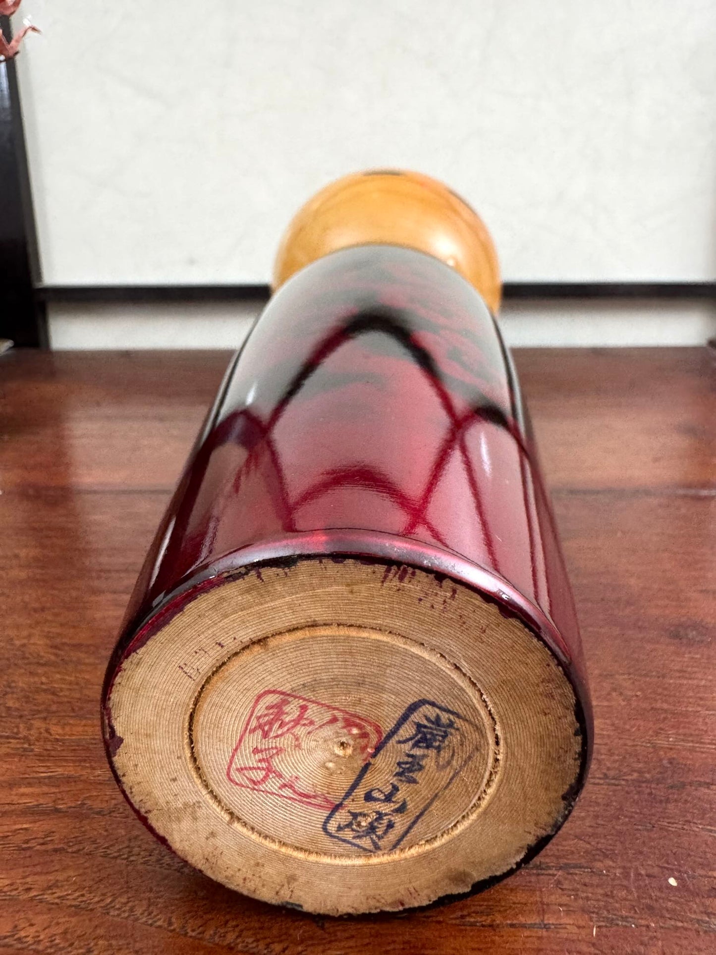 Kokeshi vintage de Sato Norio en laque noire et rouge avec branche de prunier en fleurs, vu du dessous la signature de l'artisan