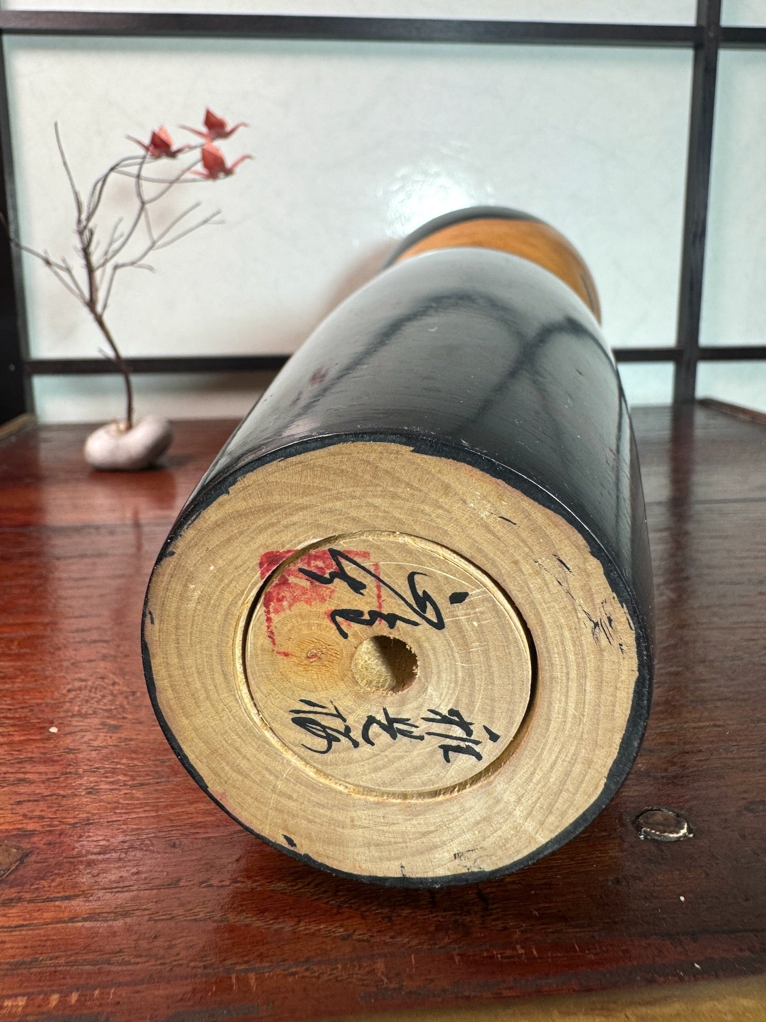 kokeshi de Watanabe Masao, nommé Shigo Sakura, corps laqué reflet rouge évoquant les cerisiers, tête cheveux noir, traits noirs pour les yeux, vu de dessous signature de l'artisan