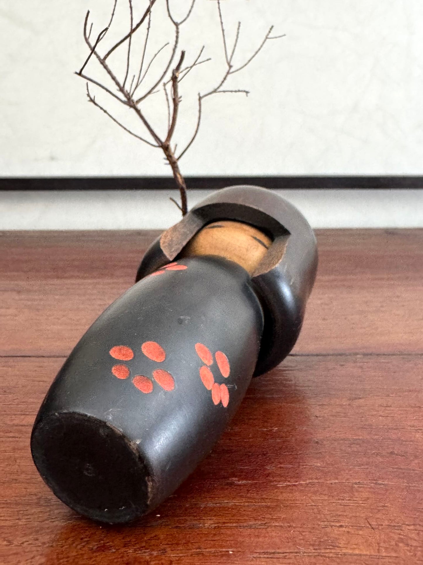 Petite kokeshi Usaburo en bois brun foncé ornée de fleurs de prunier rouge, le dessous