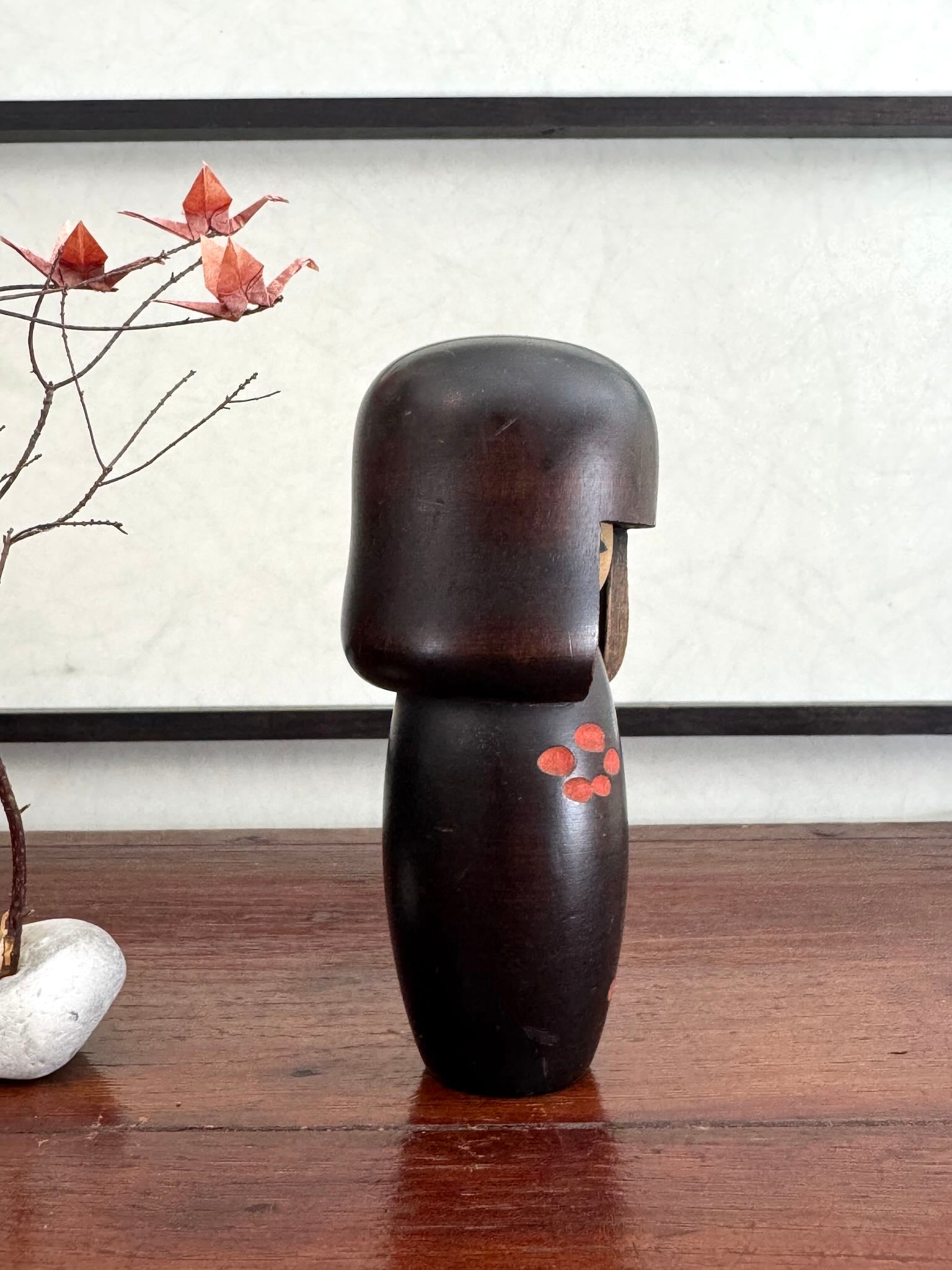 Petite kokeshi Usaburo en bois brun foncé ornée de fleurs de prunier rouge, profil droit