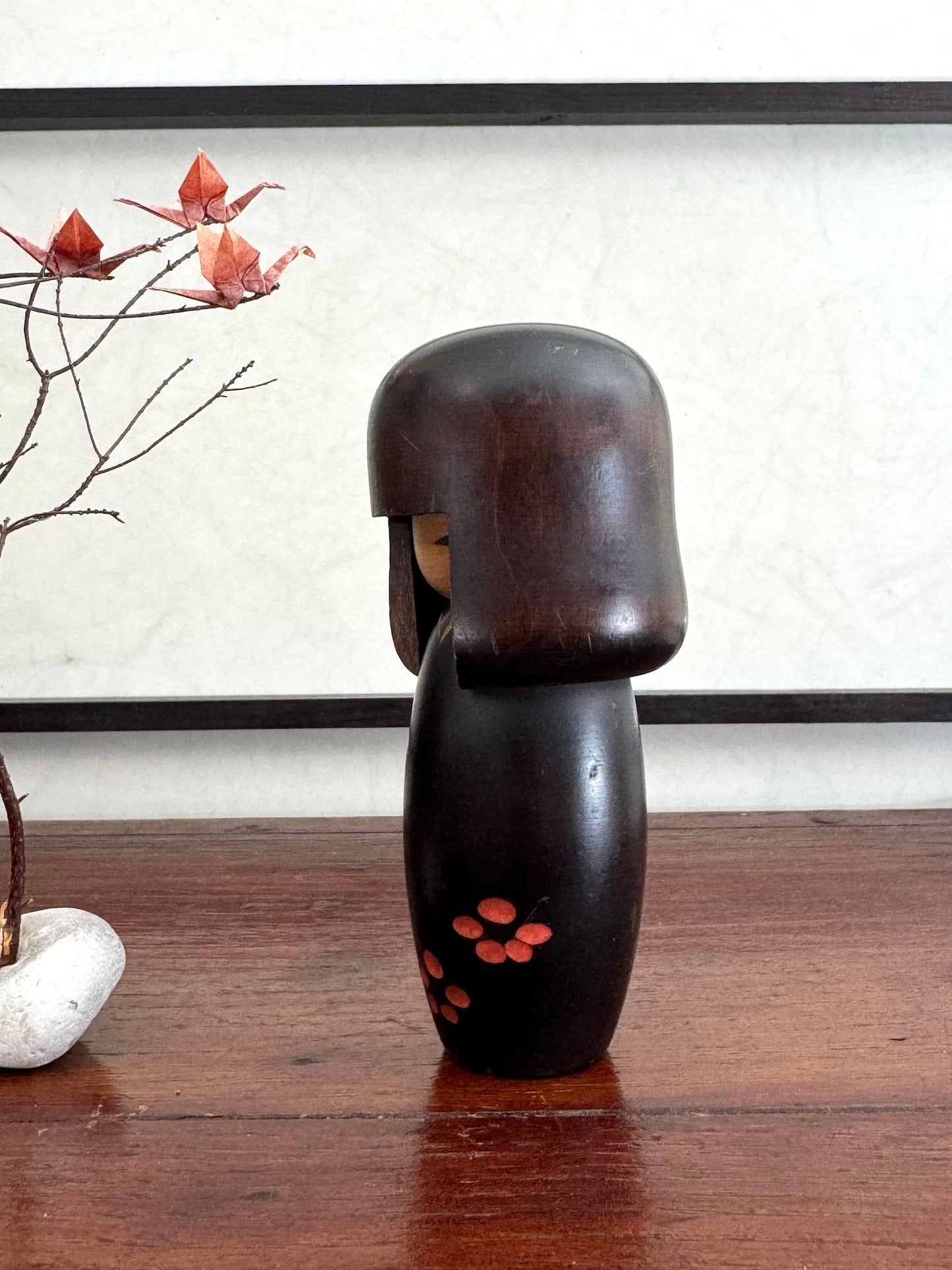 Petite kokeshi Usaburo en bois brun foncé ornée de fleurs de prunier rouge, profil gauche