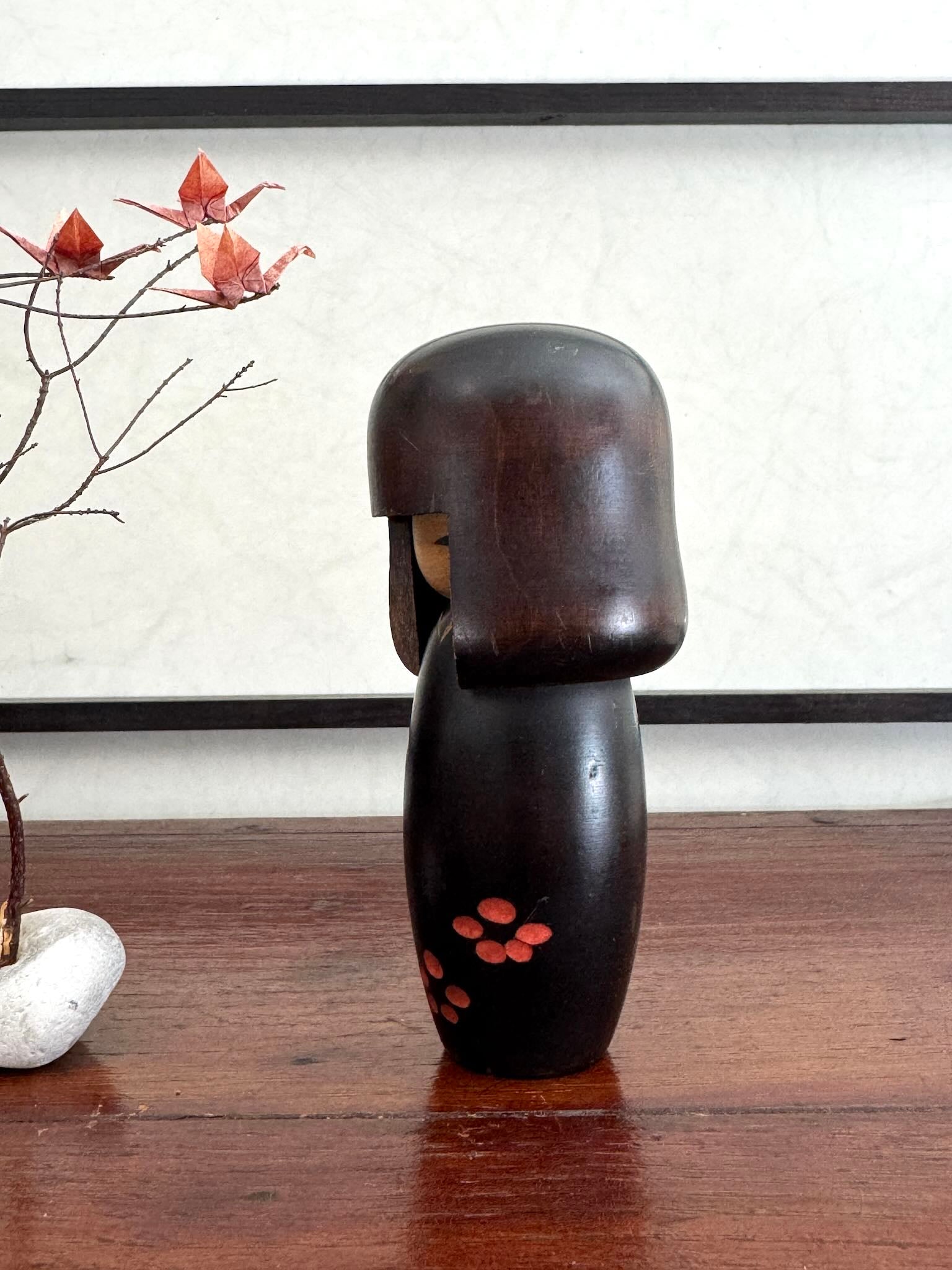 Petite kokeshi Usaburo en bois brun foncé ornée de fleurs de prunier rouge, profil gauche