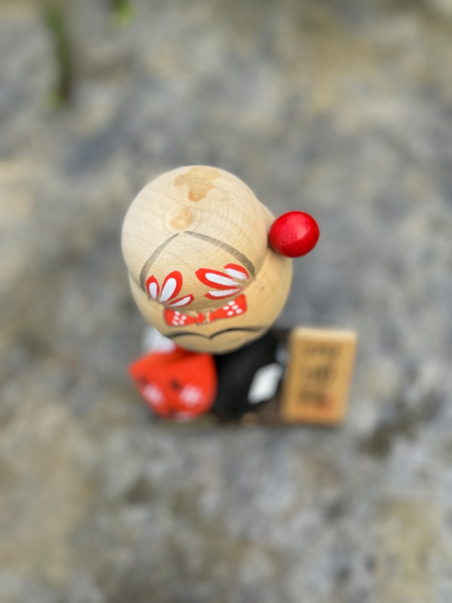 Kokeshi souvenir, poupée en bois japonaise, kimono orange et chapeau noir et blanc, pèlerinage de shikoku, épingle à cheveux rouge ronde, ruban peint et fleurs blanches sur chignon. Chignon vu de haut.
