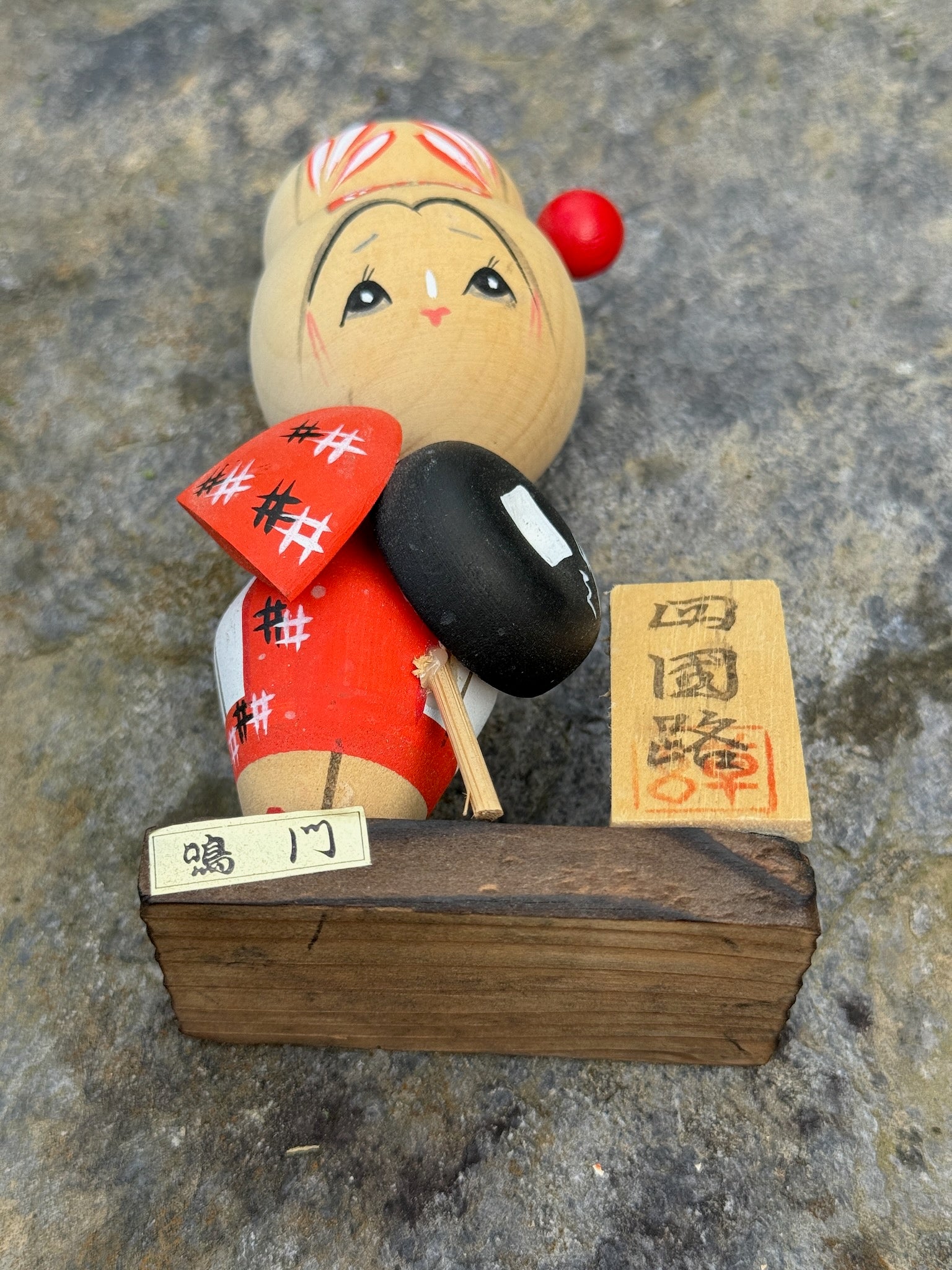 Kokeshi souvenir, poupée en bois japonaise, kimono orange et chapeau noir et blanc, pèlerinage de shikoku, épingle à cheveux rouge ronde, ruban peint et fleurs blanches sur chignon, bâton de marche. Socle dessous avec étiquette et pancarte. 