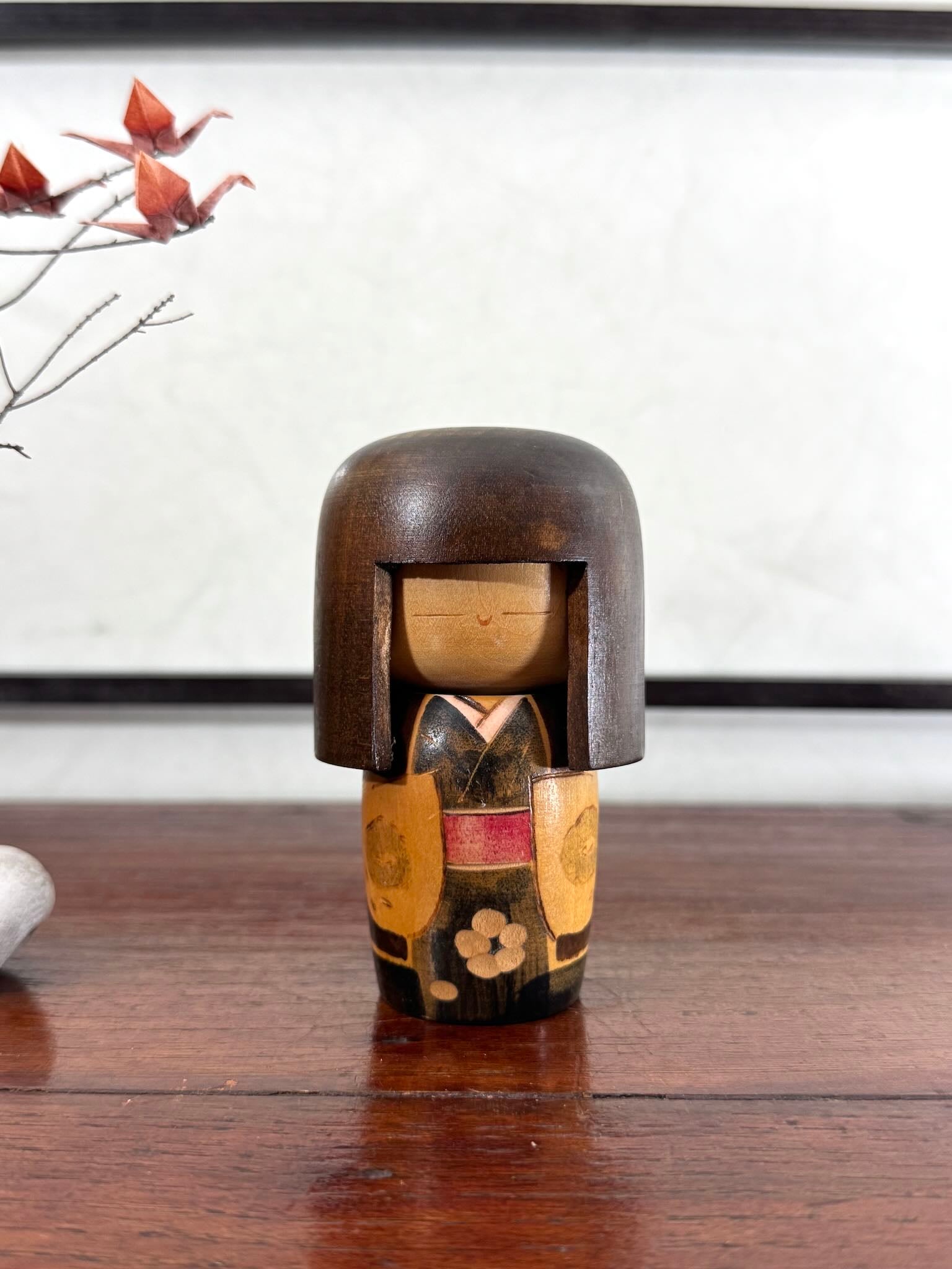Petite kokeshi Gunma Ozawa Shiun en bois avec longue chevelure brune, kimono brun avec fleurs et obi rouge, de face