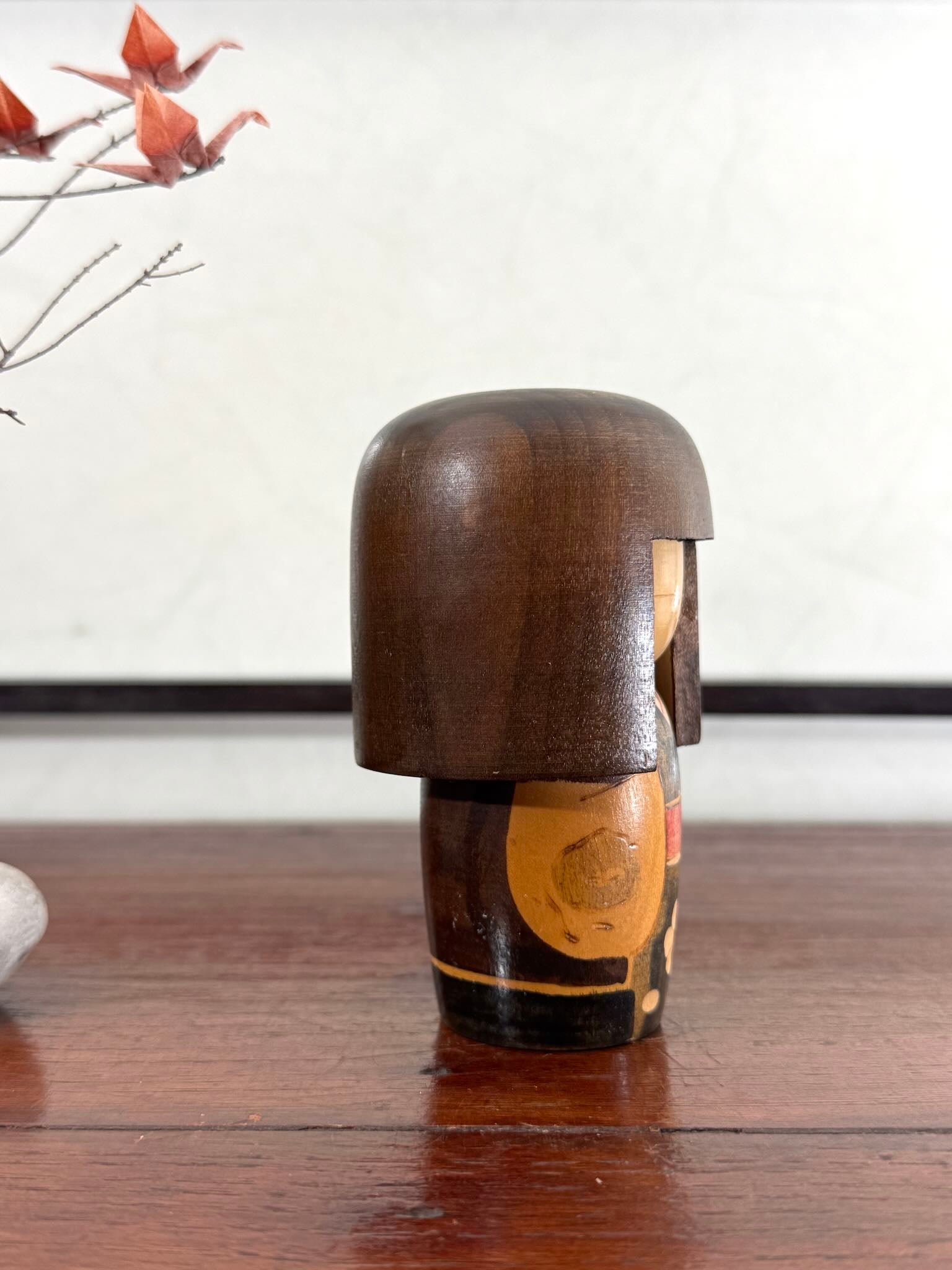 Petite kokeshi Gunma Ozawa Shiun en bois avec longue chevelure brune, kimono brun avec fleurs et obi rouge, profil droit