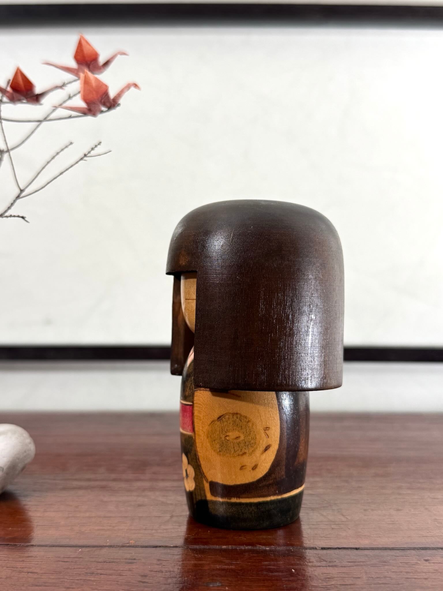 Petite kokeshi Gunma Ozawa Shiun en bois avec longue chevelure brune, kimono brun avec fleurs et obi rouge, profil gauche