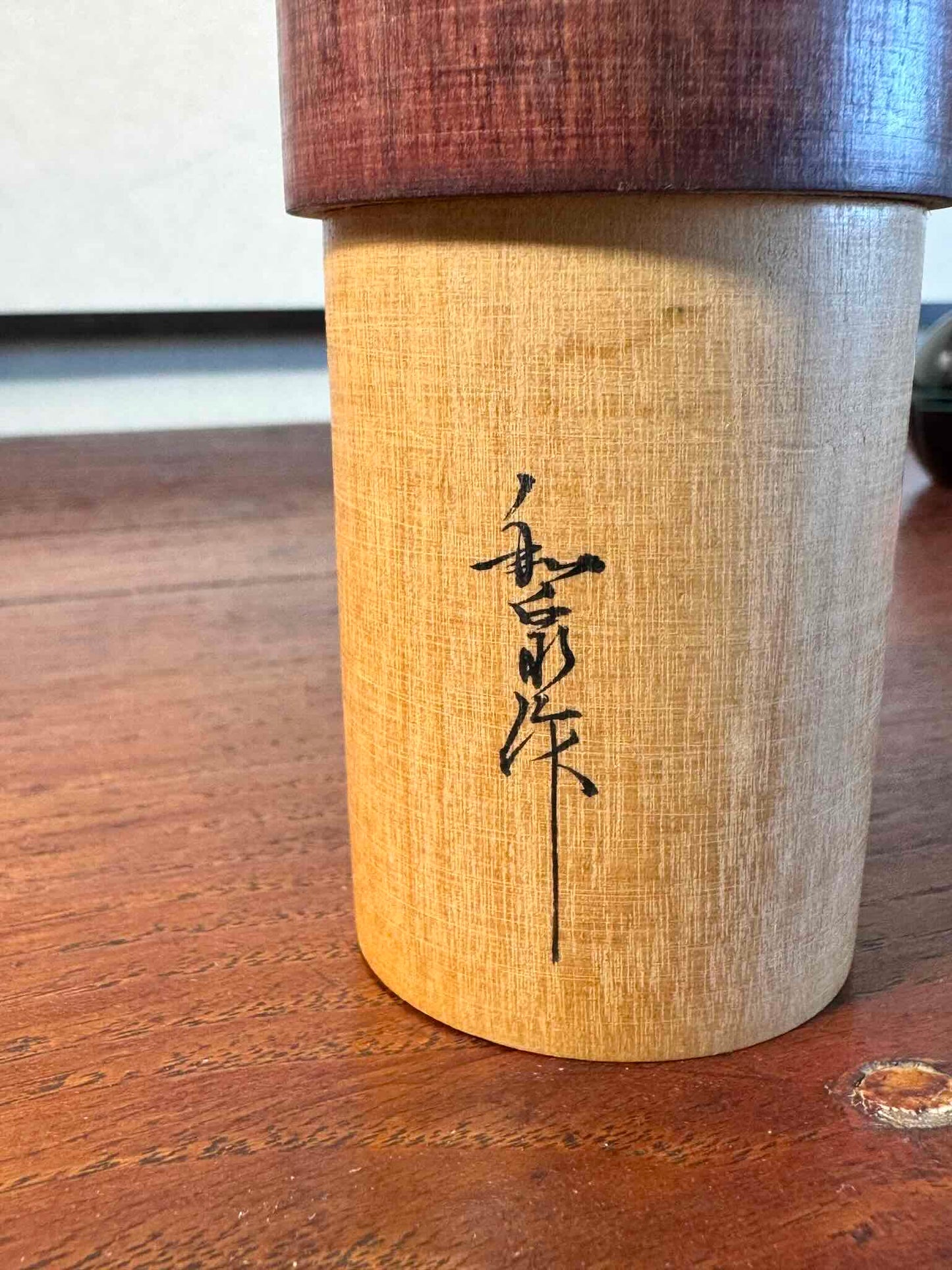 Kokeshi créative japonaise ancienne en bois naturel avec motifs floraux, gros plan sur la signature de l'artisan