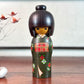 kokeshi gunma de Sadao Kishi au kimono vert, fleurs stylisées et obi rouge à carreaux