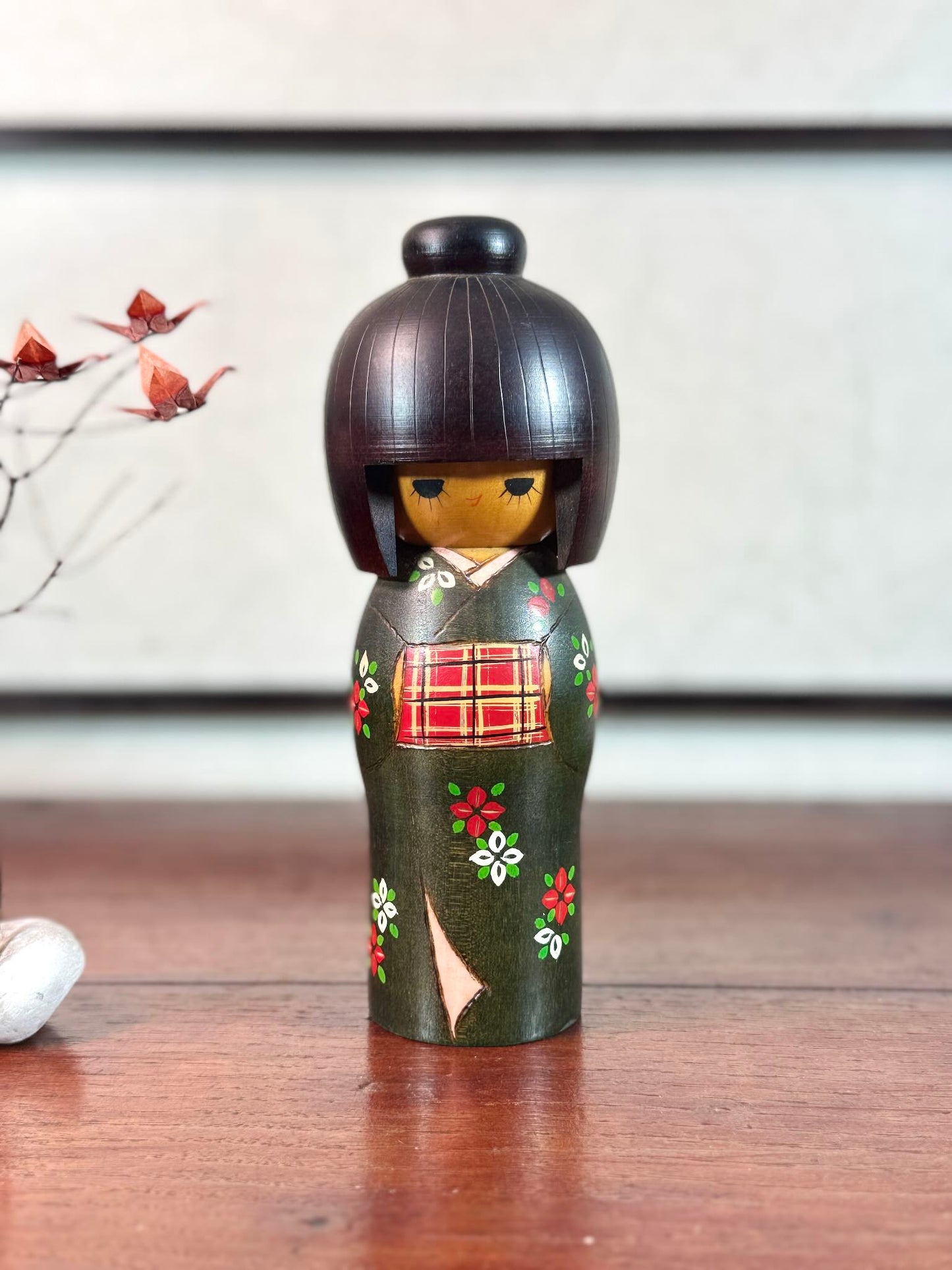 kokeshi gunma de Sadao Kishi au kimono vert, fleurs stylisées et obi rouge à carreaux