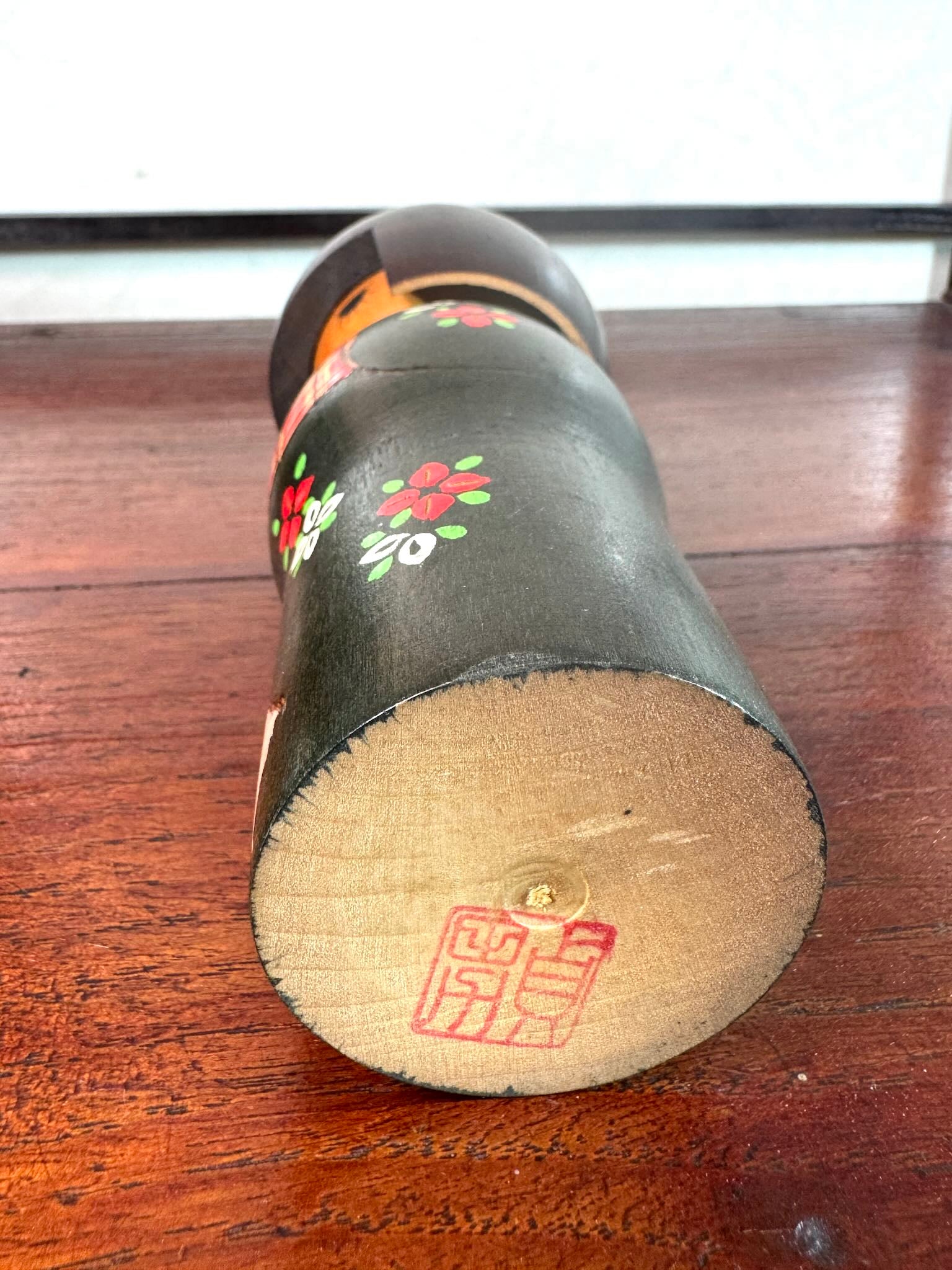 kokeshi gunma de Sadao Kishi au kimono vert, fleurs stylisées et obi rouge à carreaux, a signature de l'artisan au dessous