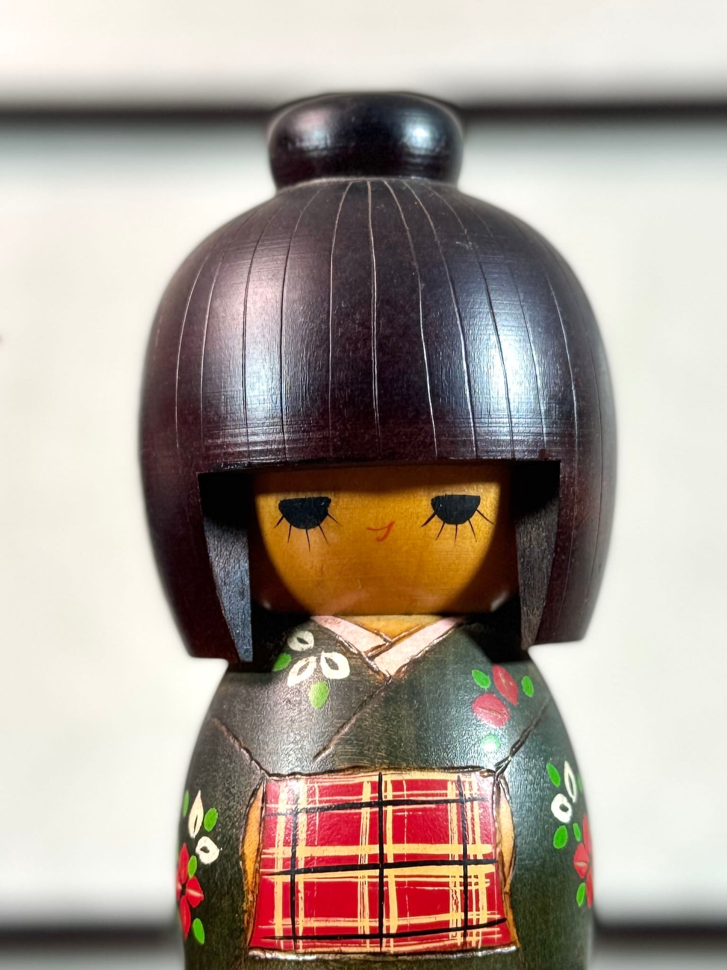 kokeshi gunma de Sadao Kishi au kimono vert, fleurs stylisées et obi rouge à carreaux, gros plan sur le visage souriant
