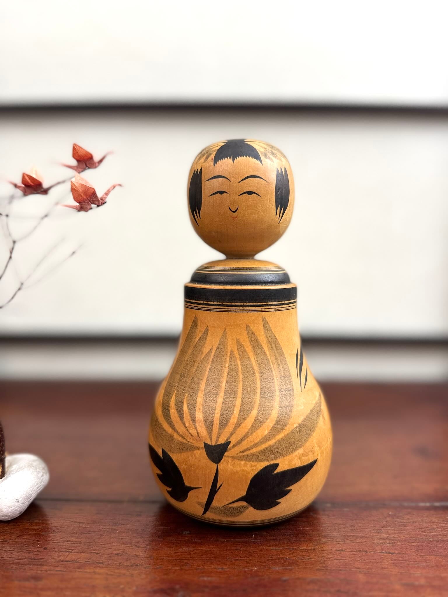 Poupée Japonaise Kokeshi nemariko de Sato Yoshihiro, avec un grand chrysanthème noir peint à la main, vu d, vu de face.