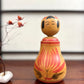 Poupée Japonaise Kokeshi nemariko de Sato Yoshihiro, avec un grand chrysanthème rouge peint à la main, vu de face