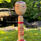 kokeshi poupée japonaise aux grands yeux cernés de rose et à l'expression étonnée