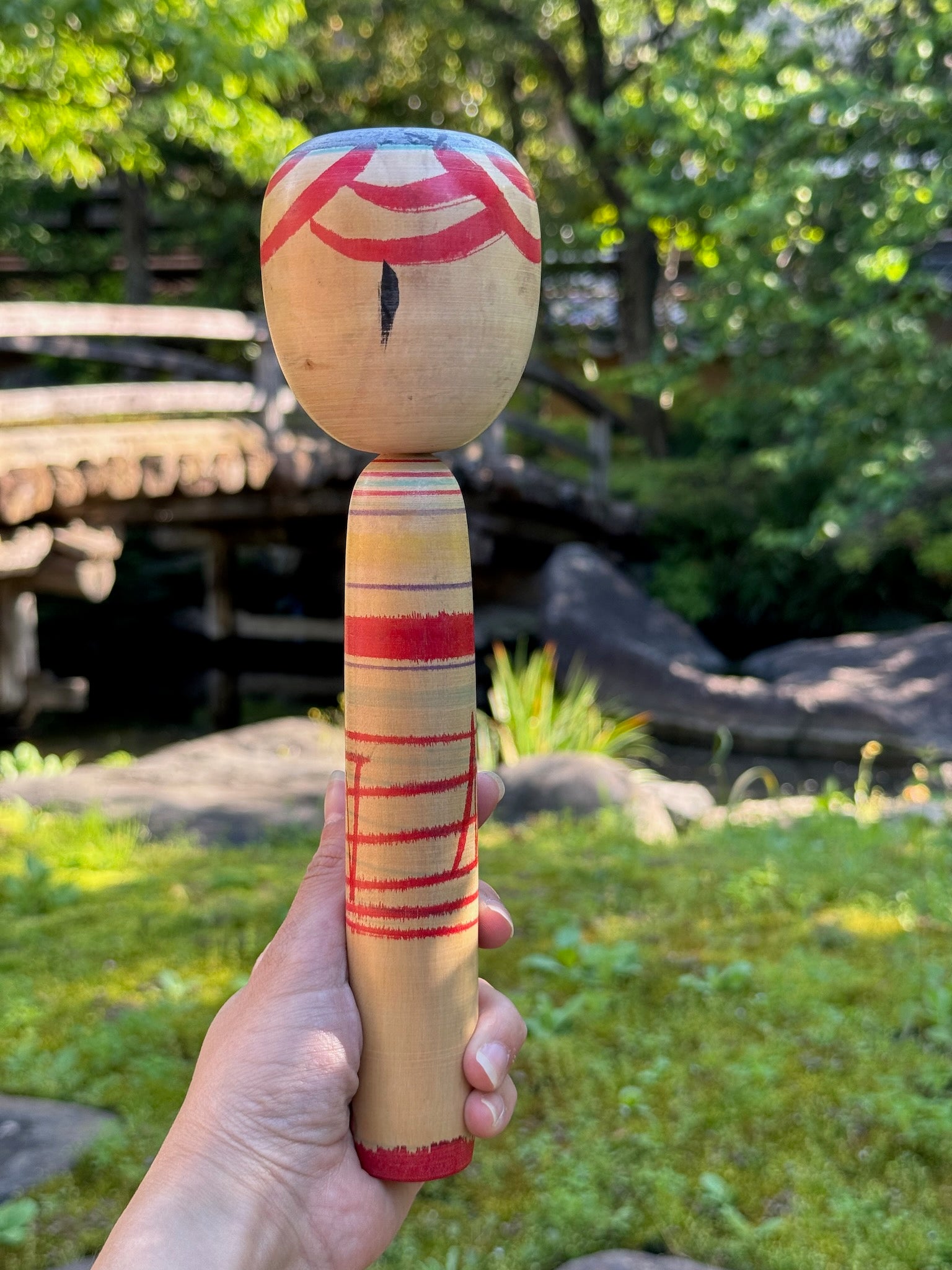 kokeshi poupée japonaise aux grands yeux cernés de rose et à l'expression étonnée, vu de dos