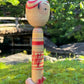 kokeshi poupée japonaise aux grands yeux cernés de rose et à l'expression étonnée, profil droit