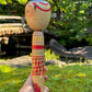 kokeshi poupée japonaise aux grands yeux cernés de rose et à l'expression étonnée, profil gauche