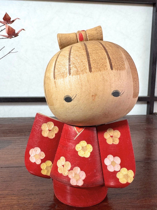 Kokeshi japonaise rouge avec fleurs, coiffée d’un nœud, signée Kazuo Takamizawa