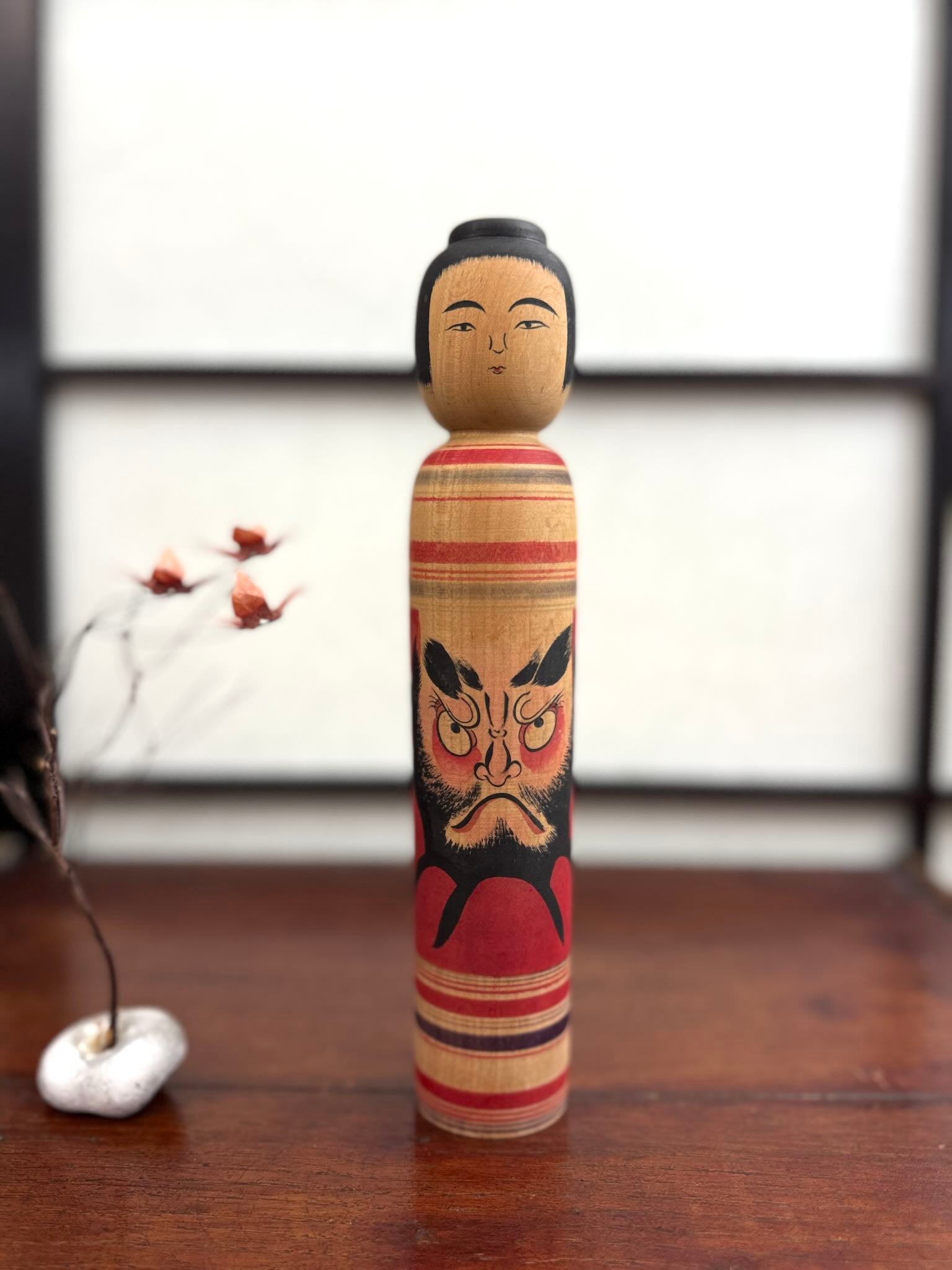 Kokeshi vintage Junichi Sasamori style Kohei avec visage de Daruma rouge et noir, de face.
