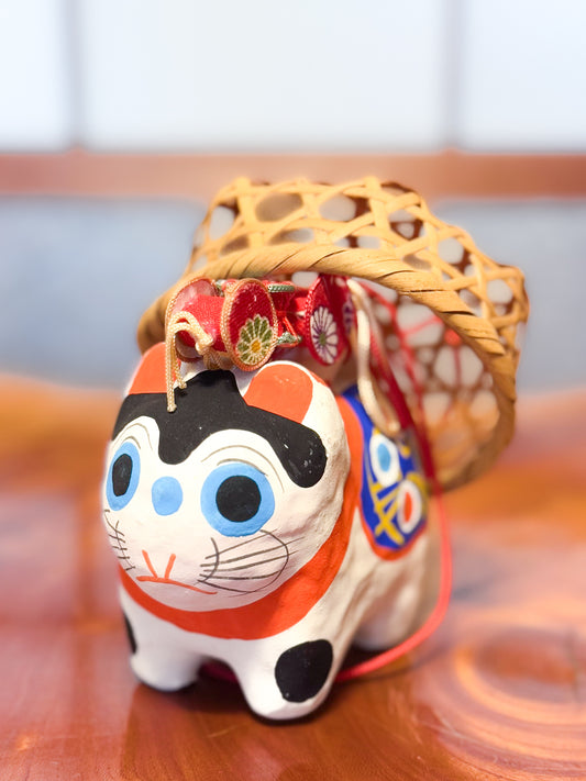 Figurine japonaise en papier mâché représentant un inu hariko blanc décoré, avec panier en bambou et tambours miniatures sur le dos, vu de face