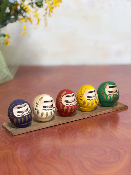 Ensemble de cinq Daruma colorés sur socle en bois