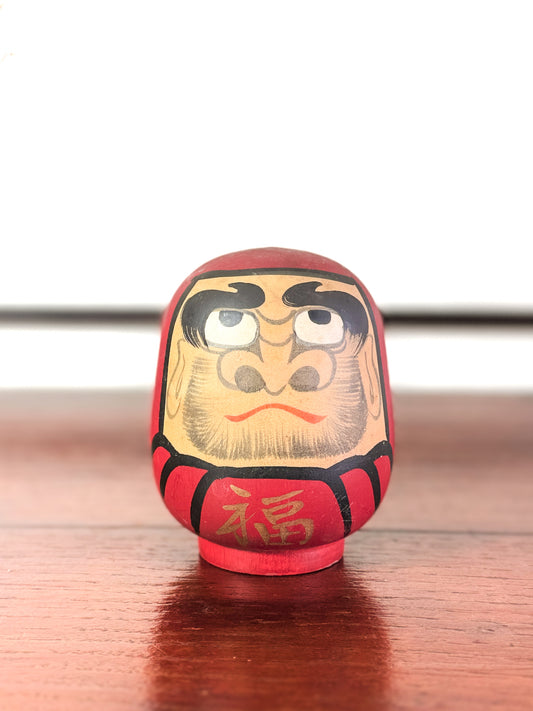 Daruma rouge en bois avec visage peint et caractère doré 福 sur le torse