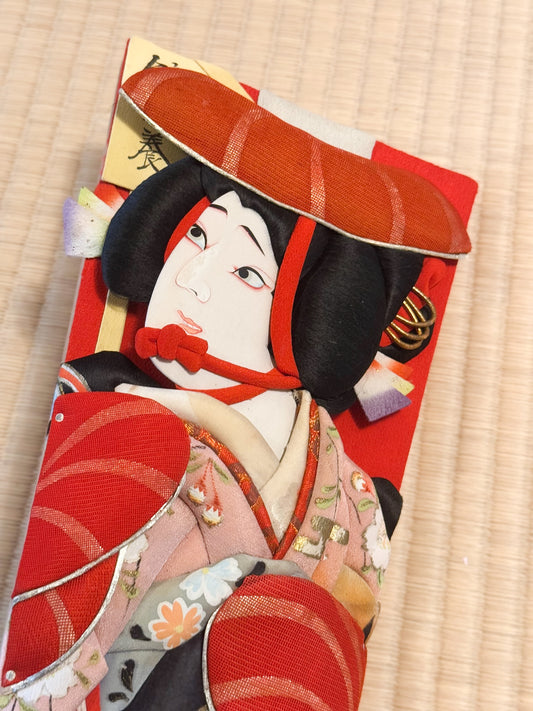 Hagoita, raquette japonaise en bois et tissu avec visage de femme en relief, gros plan