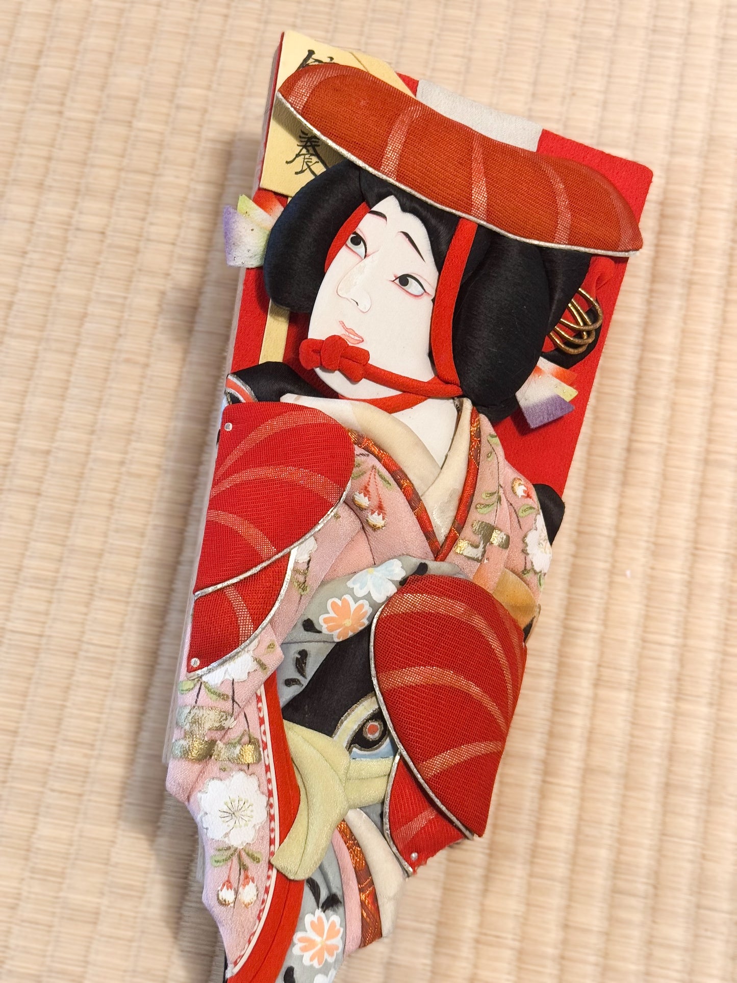 Hagoita, raquette japonaise en bois et tissu avec visage de femme en relief, vu de dessus