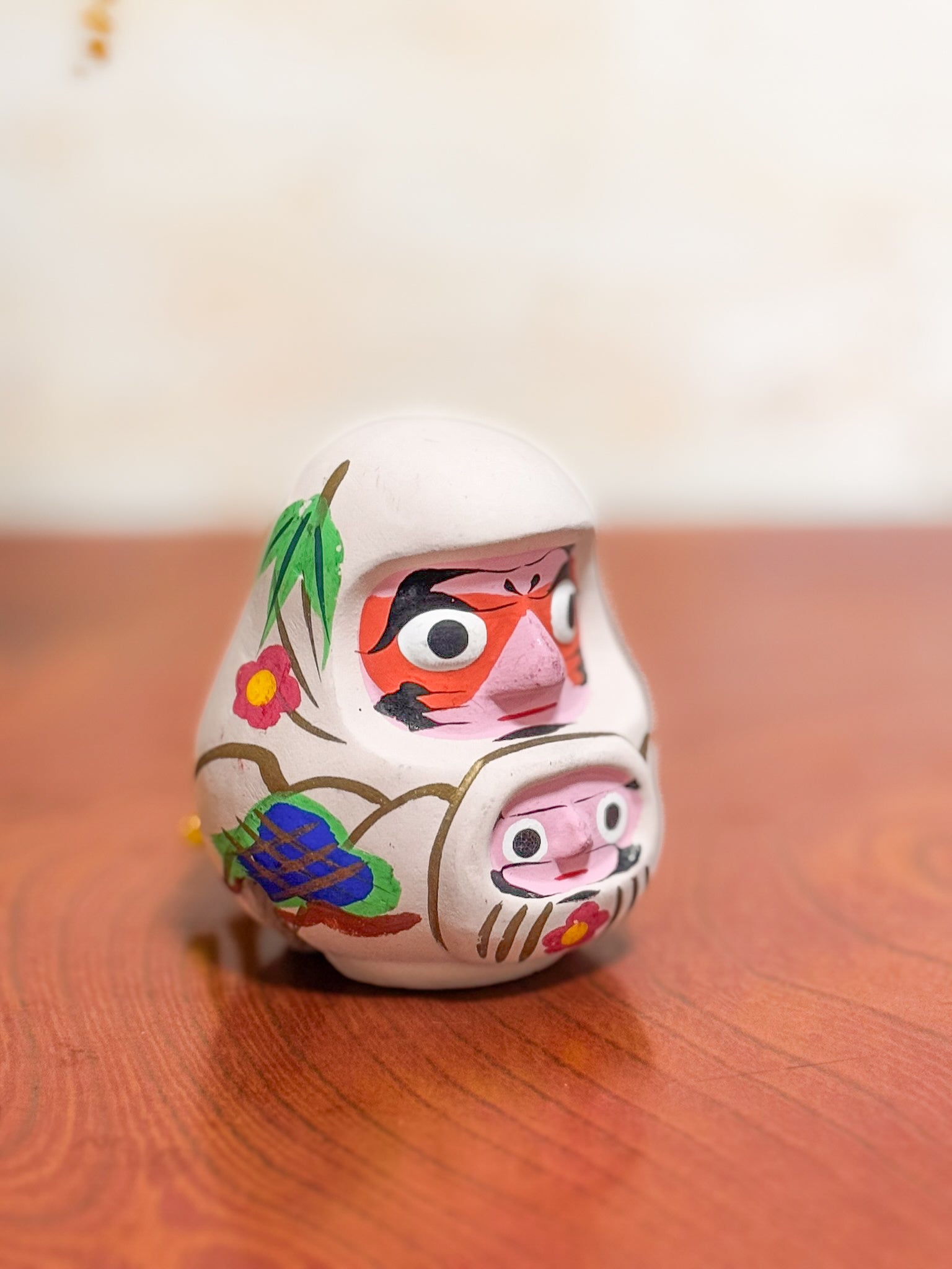 Clochette japonaise en terre cuite peinte à la main représentant deux daruma, adulte et enfant, ornée de fleurs et motifs traditionnels, vu de 3/4 droite