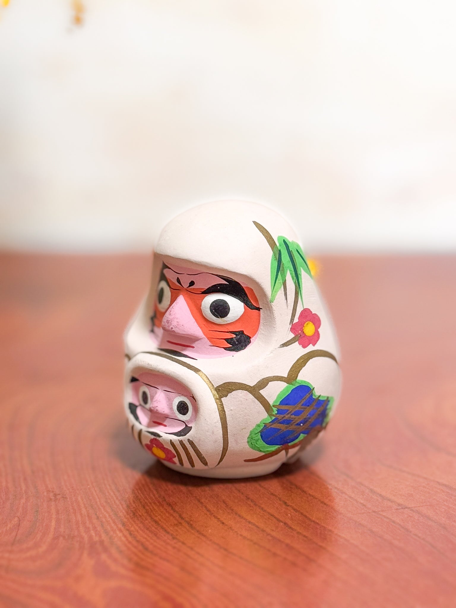 Clochette japonaise en terre cuite peinte à la main représentant deux daruma, adulte et enfant, ornée de fleurs et motifs traditionnels, vu de 3/4 gauche