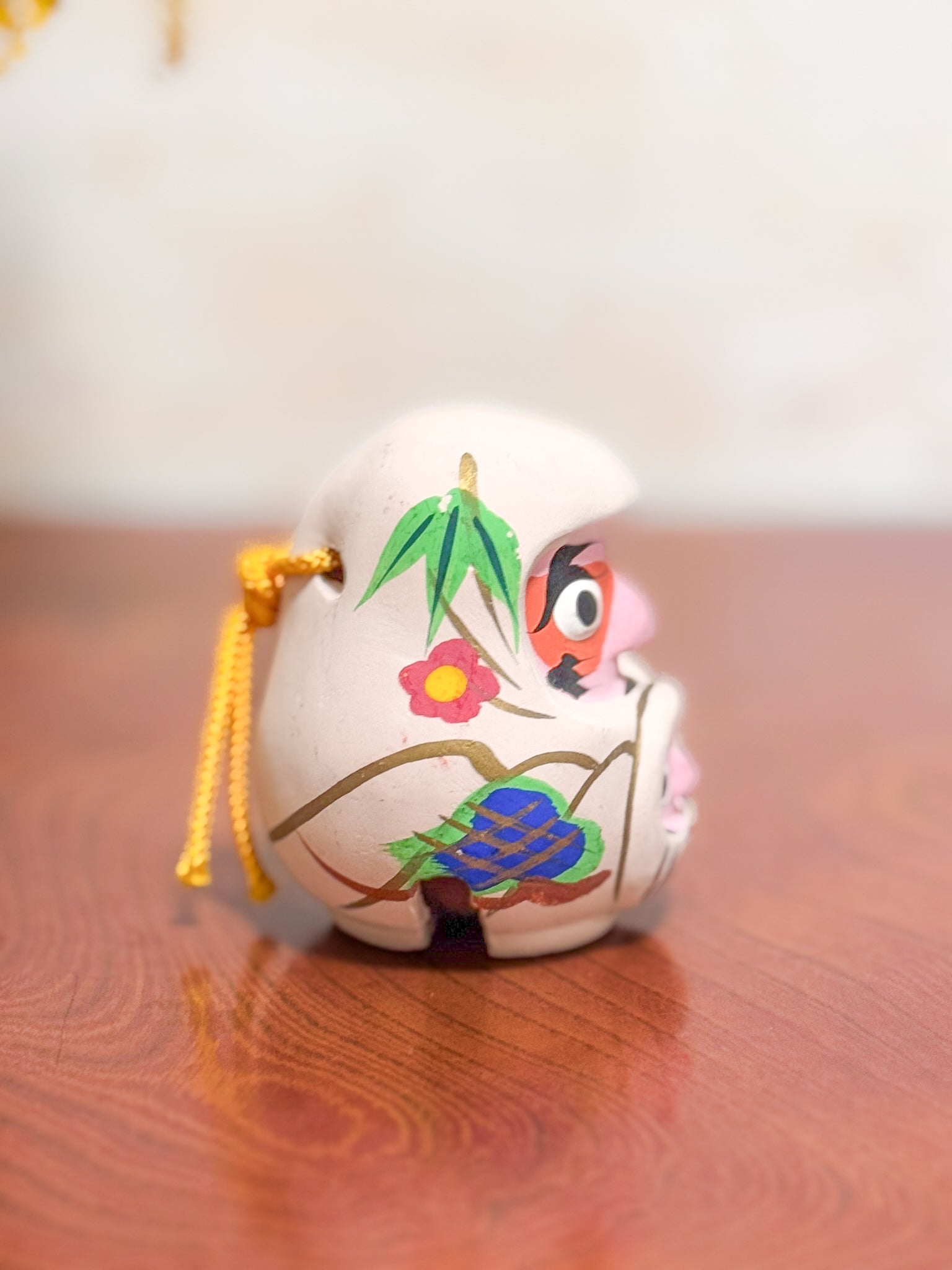 Clochette japonaise en terre cuite peinte à la main représentant deux daruma, adulte et enfant, ornée de fleurs et motifs traditionnels, profil droit
