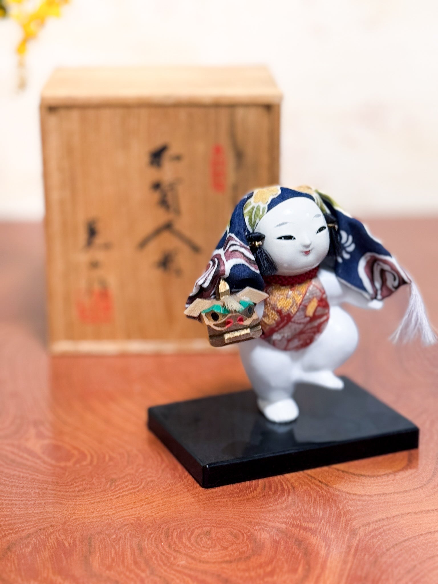 Figurine japonaise Gosho Ningyō représentant un enfant dansant avec une tête de lion Shishimai, sur socle laqué, avec boîte en bois calligraphiée, vu 3/4 gauche